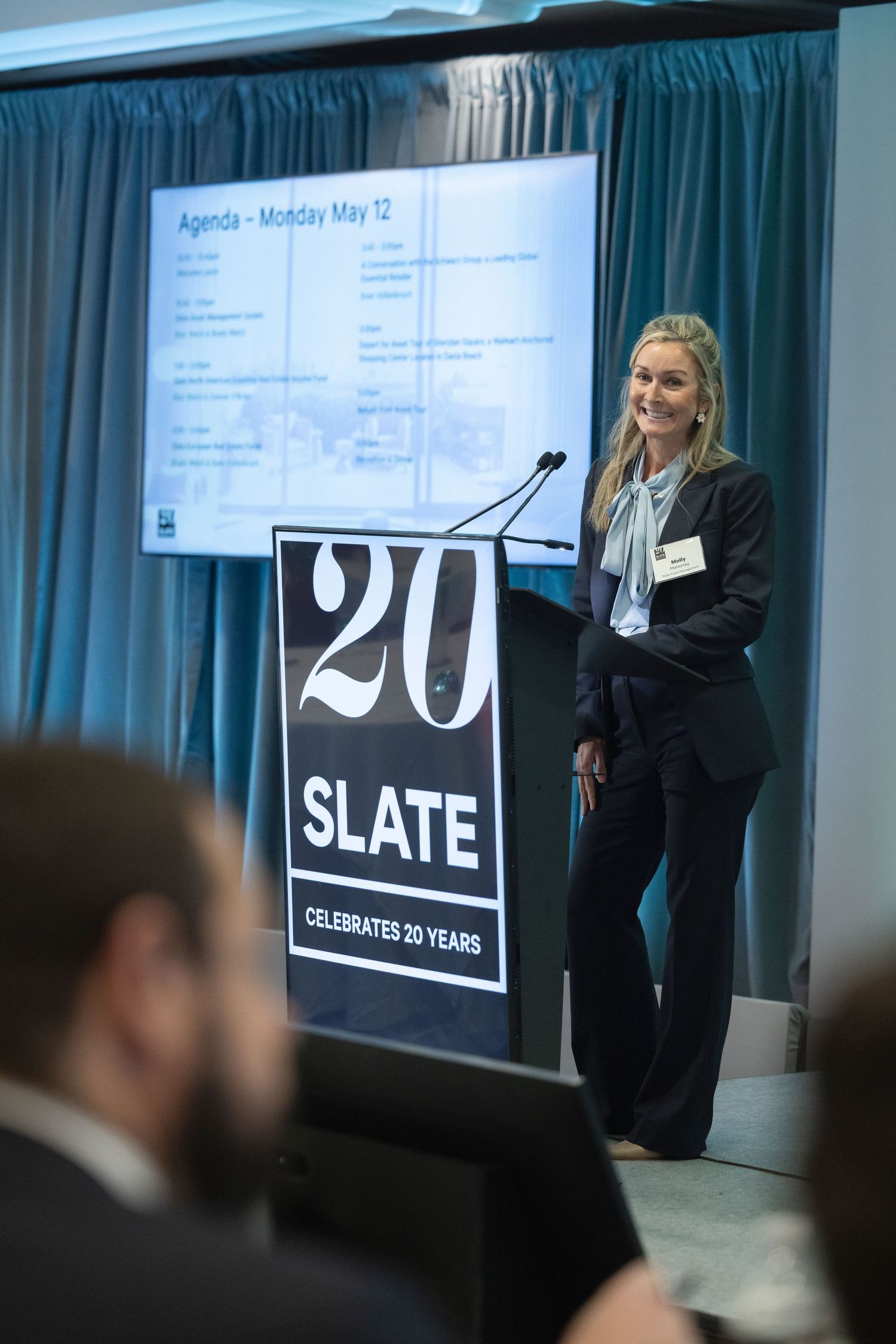 Professional business conference presentation showing SLATE branding on stage with speaker and audience.