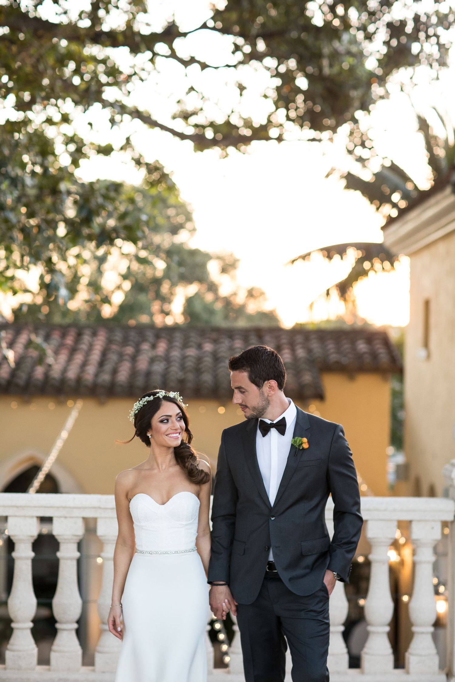 Newlyweds walking along ornate white balustrade during golden hour.
