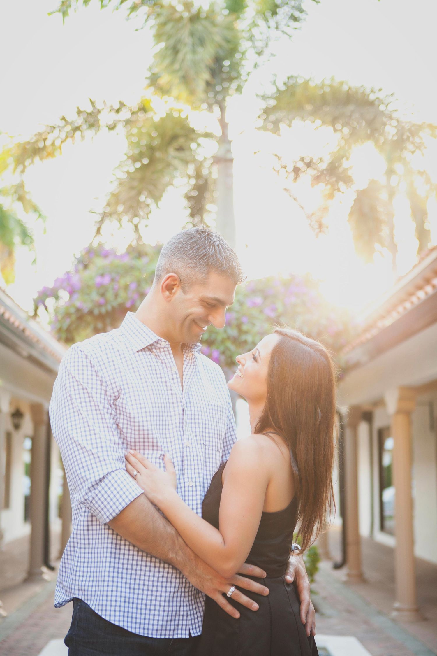 Couple embracing during a sunset photoshoot in front of Spanish-style architecture.