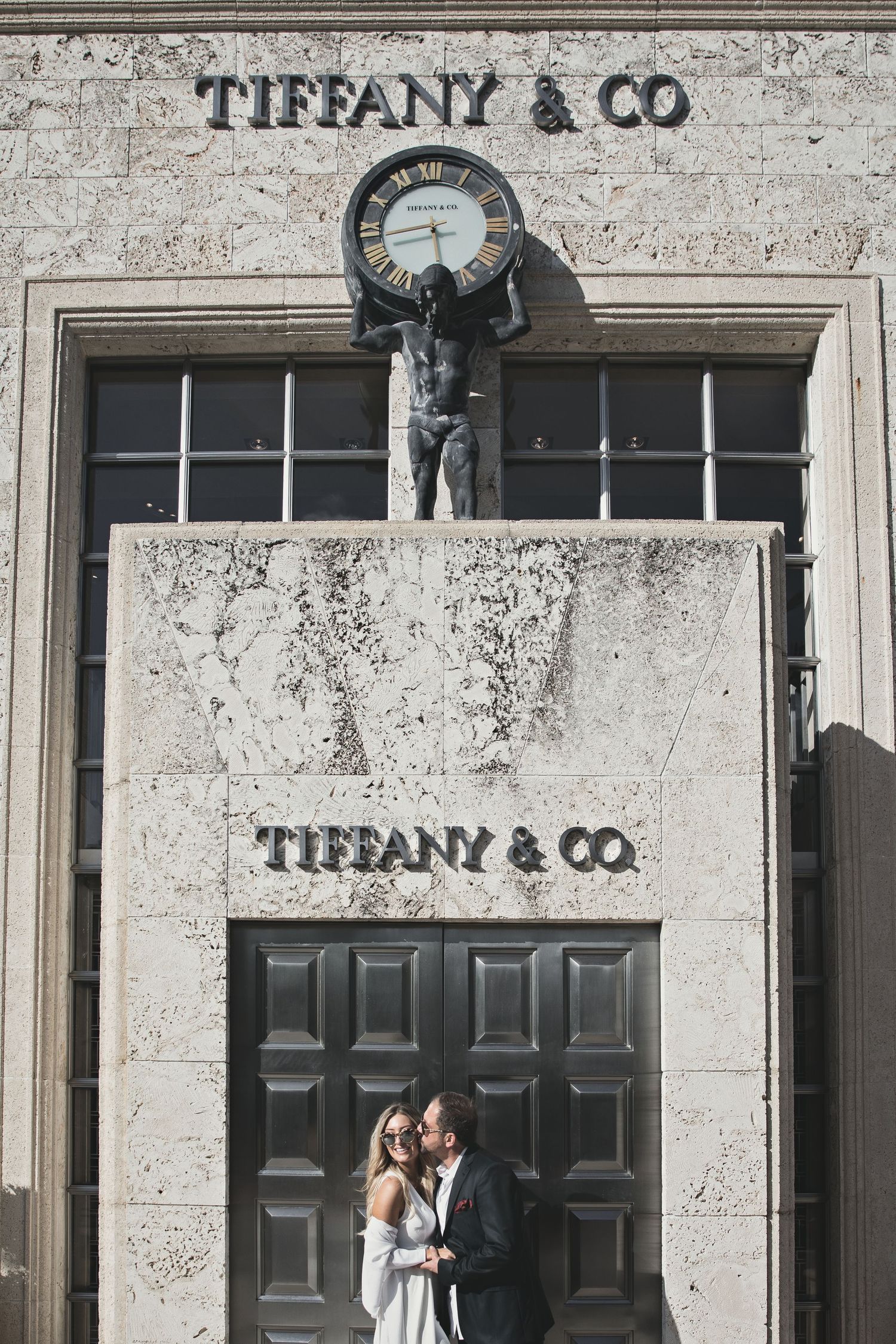 A couple poses outside the iconic Tiffany & Co storefront with classic architectural details.