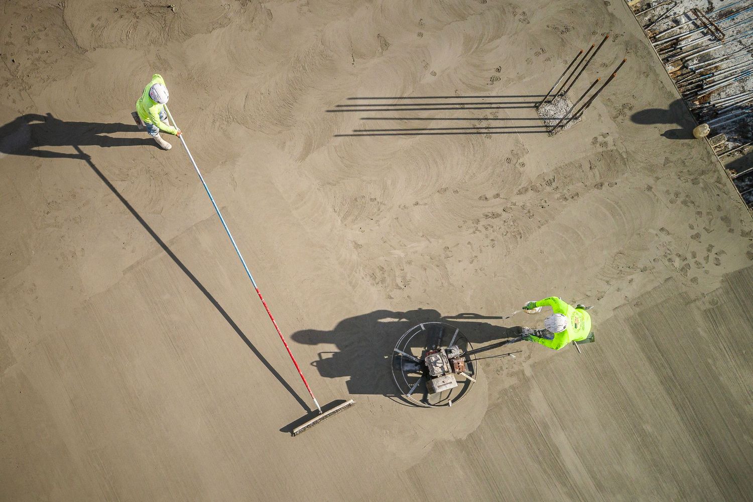 Aerial view of workers in safety vests performing utility line maintenance along a dirt path.
