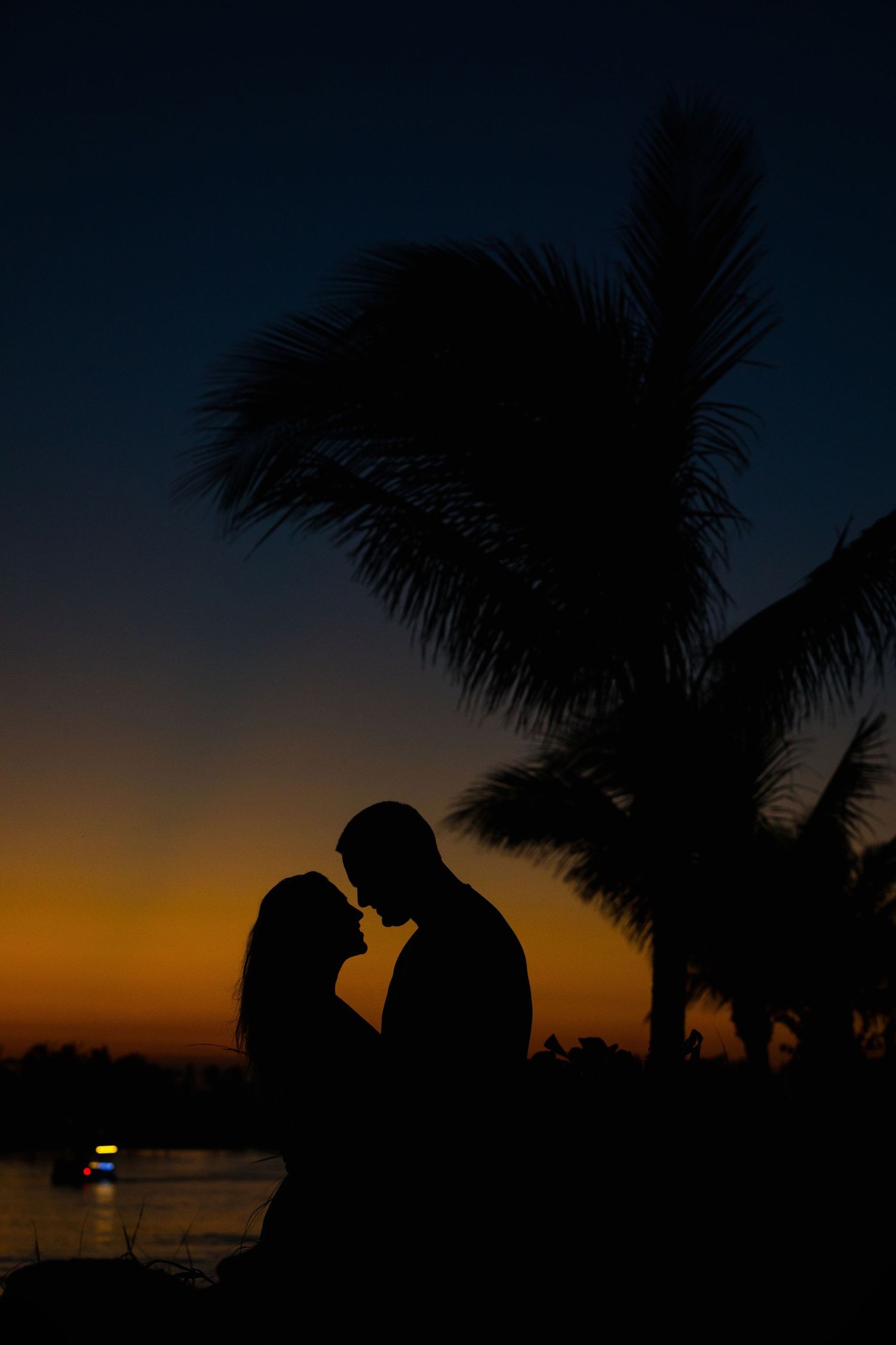 Silhouettes of a couple against a dramatic sunset sky with palm trees framing the scene.