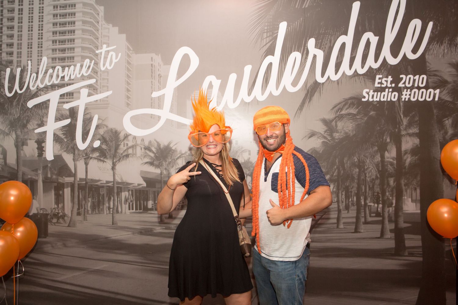 People celebrating at an event with orange balloons and black and white wall graphics in the background.