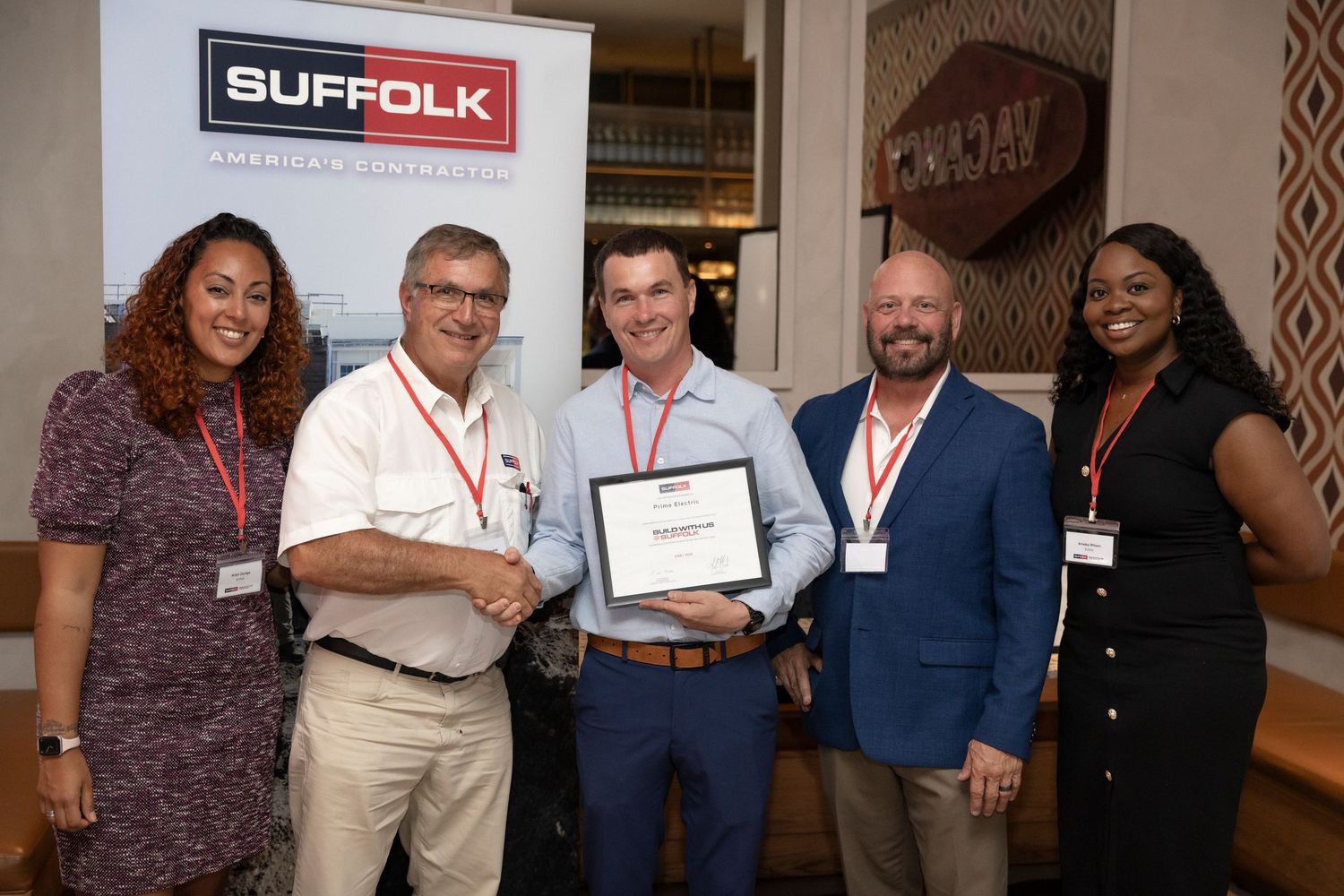 A group of people poses together at a business or professional event with certificates and name badges.