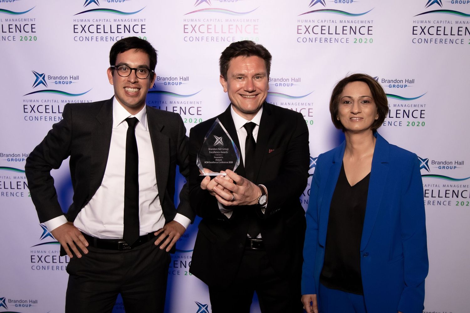 A group of people posing together at a formal event with Excellence banners visible in the background.
