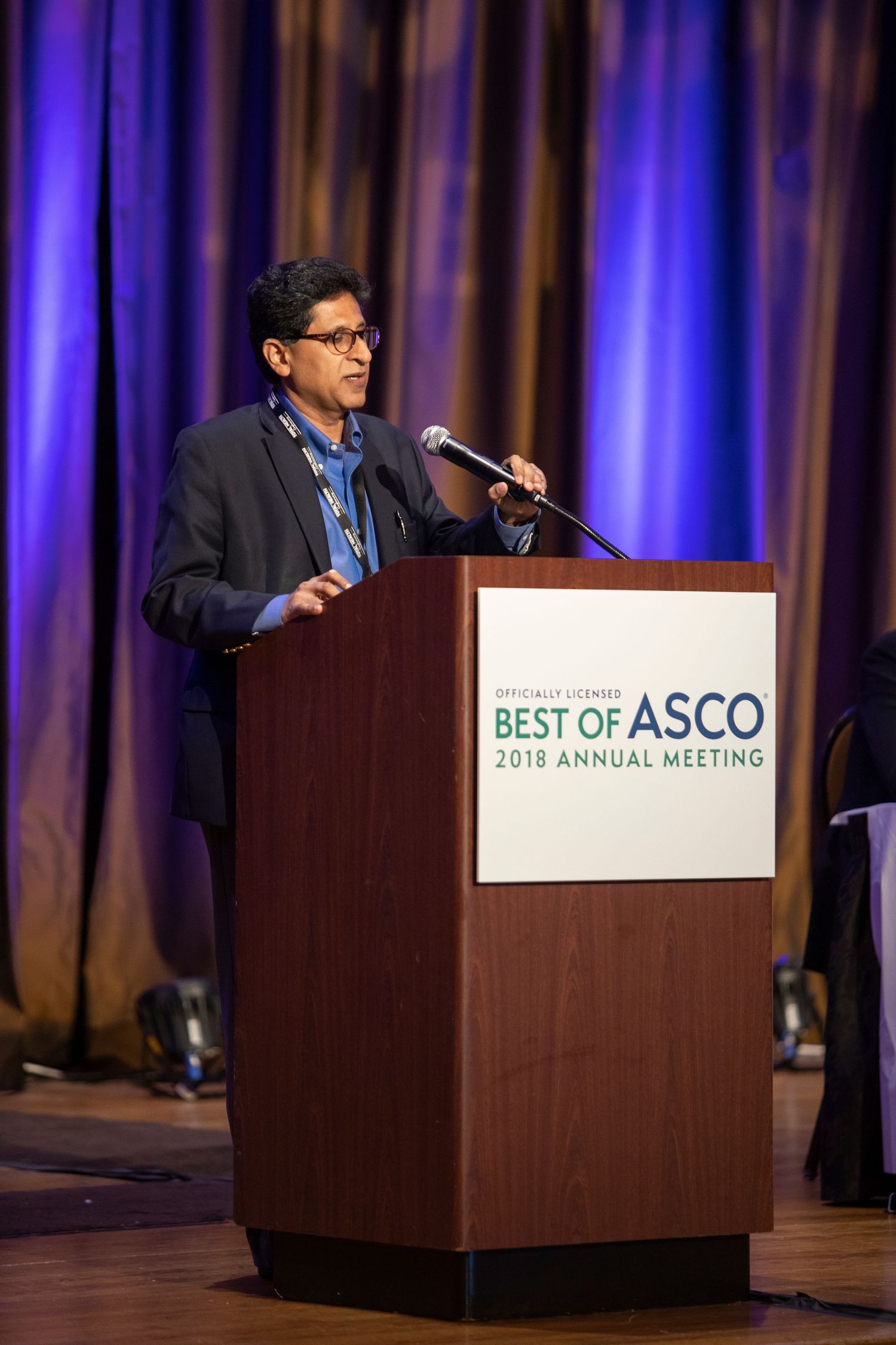 A podium with the Best of ASCO logo and blue-lit curtains in the background during a presentation.