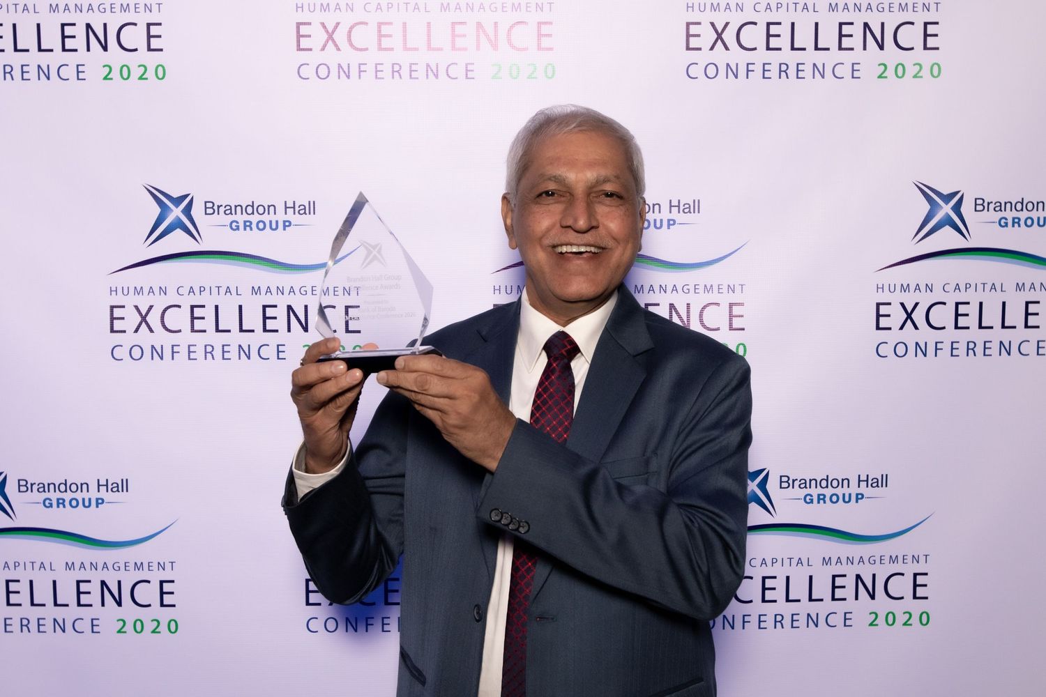Professional speaker addressing audience at the Excellence Conference with branded backdrop and energetic gestures.