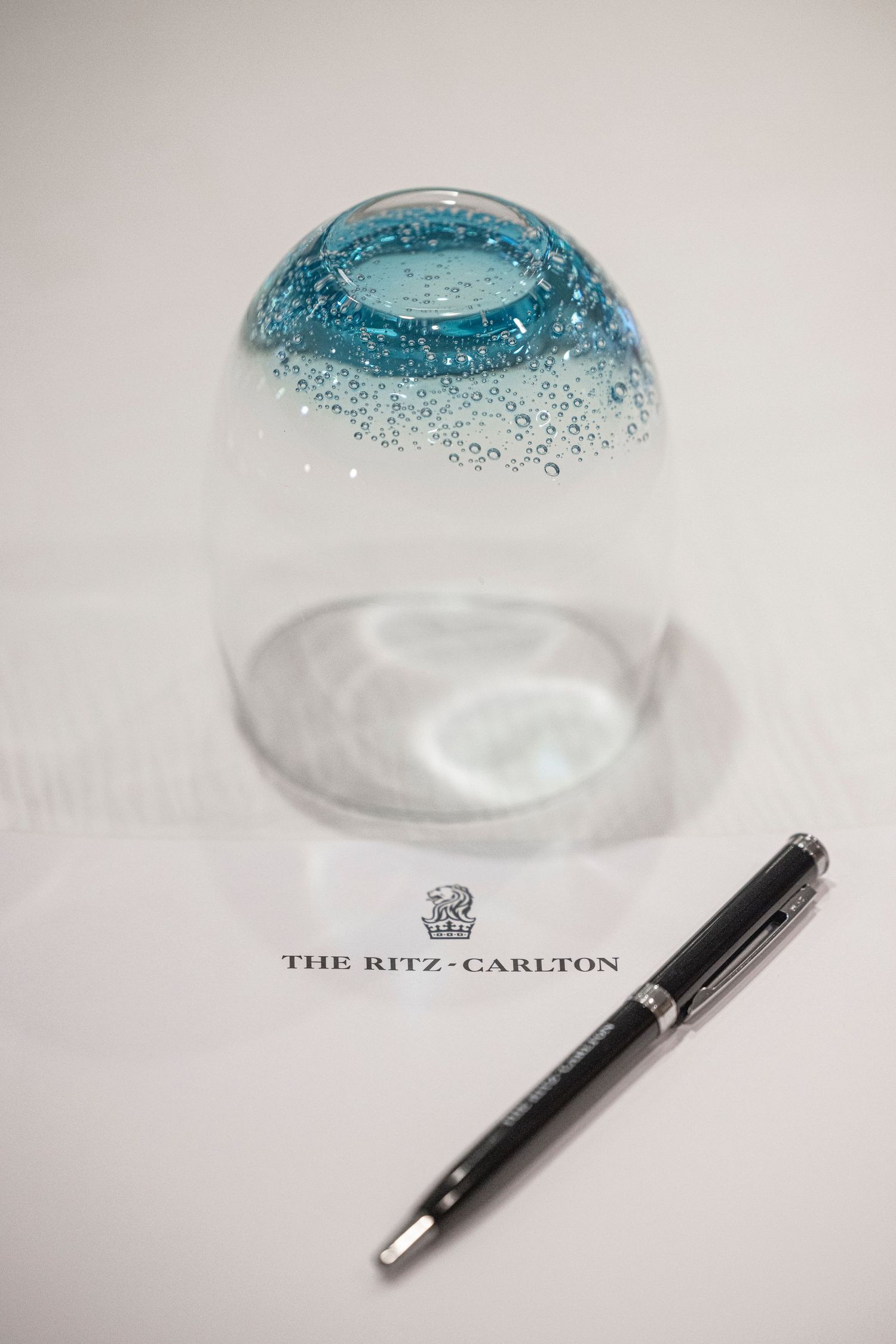 A glass snow globe and black pen on The Ritz-Carlton branded stationery featuring a blue glitter dome design.