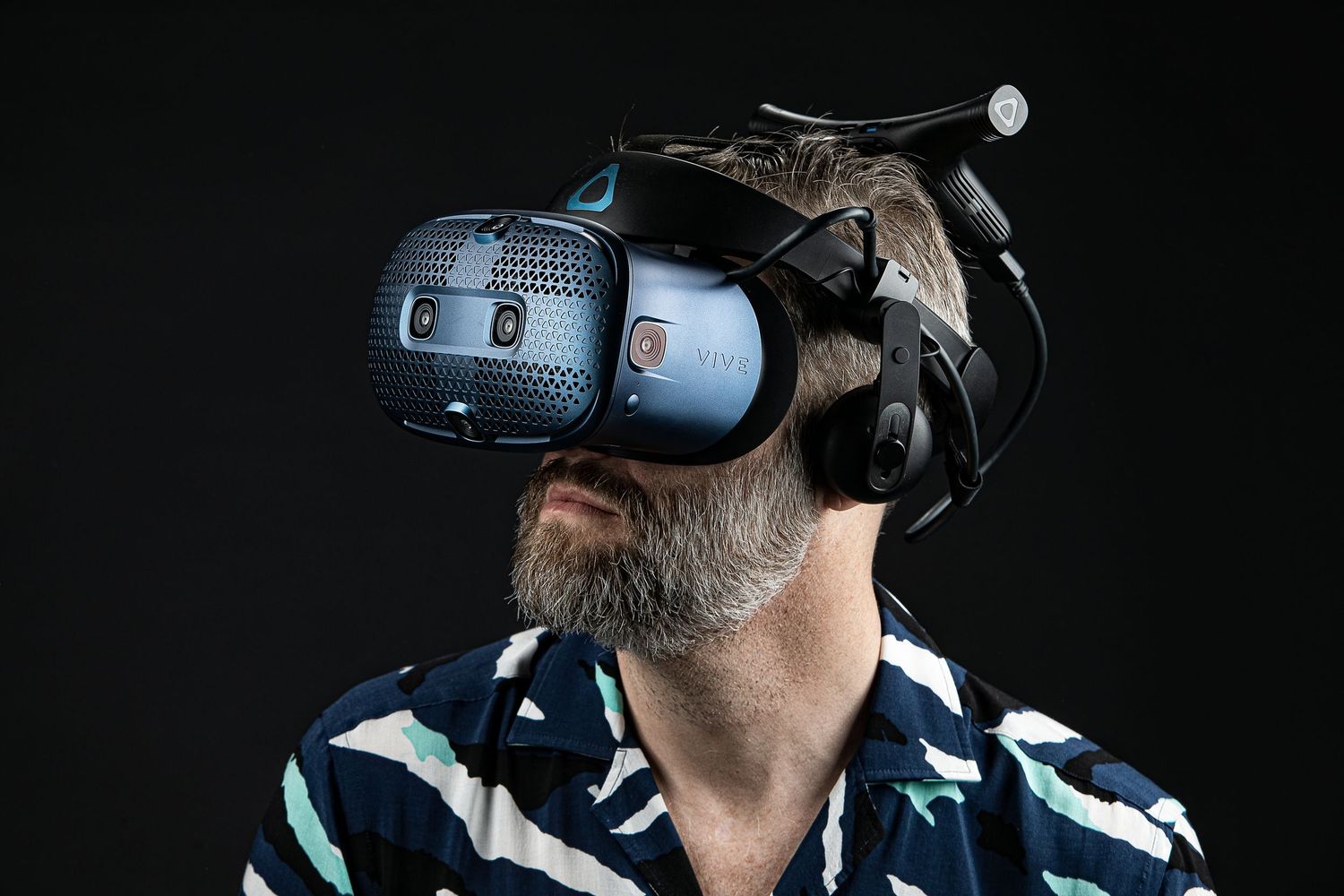 Person wearing blue HTC Vive virtual reality headset against dark background while looking up at angle.