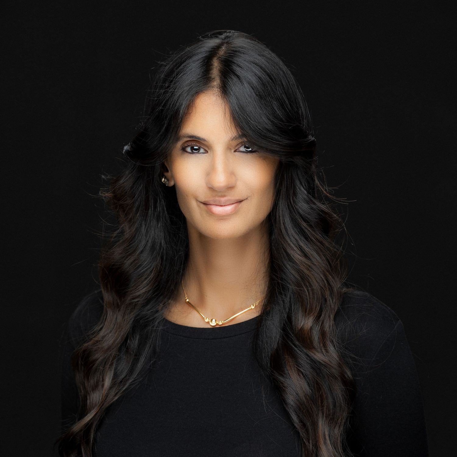 Professional portrait of a smiling woman with long dark hair wearing black against a dark background.