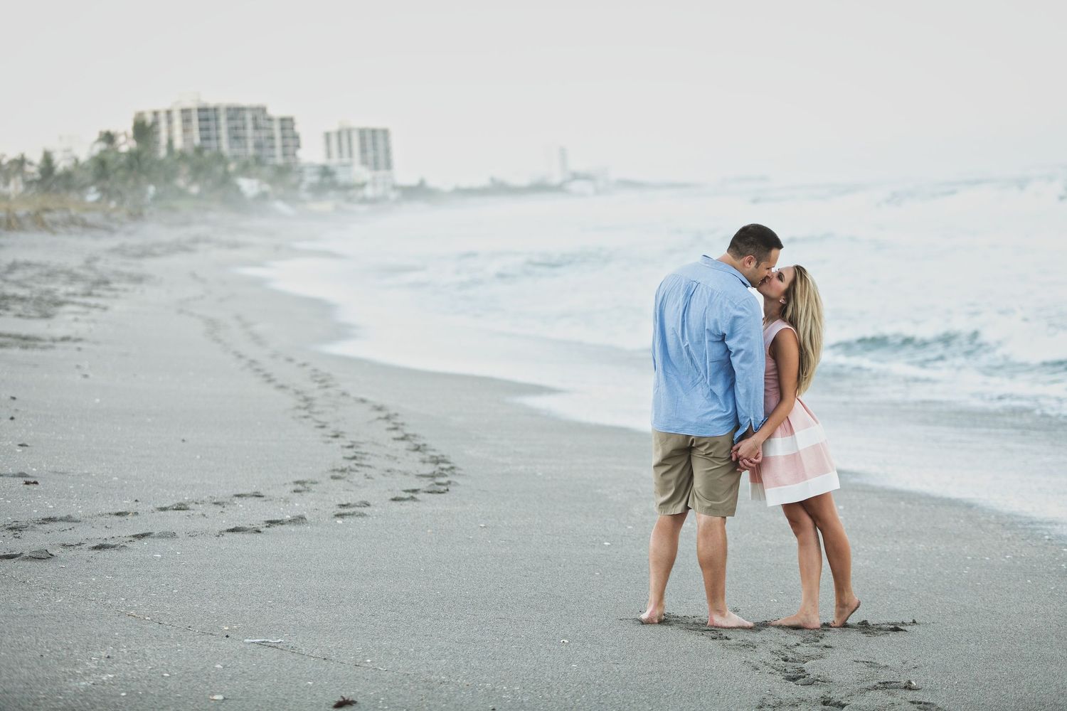 Two people write messages in the sand on a serene beach with waves in the background.