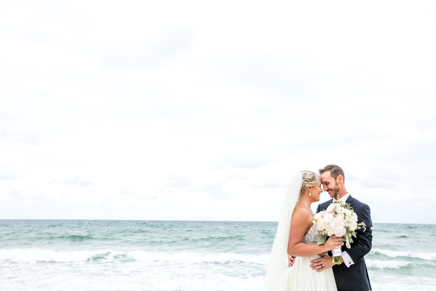 Romantic beach wedding photoshoot with waves and clouds in the background.