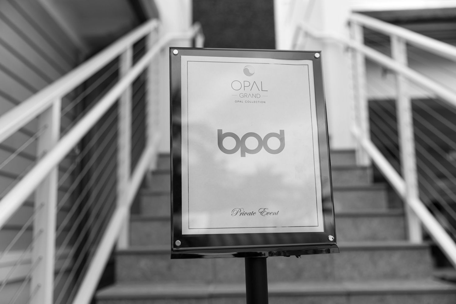 Black and white photograph showing customer table signs with calligraphy text in wooden frames at an event.