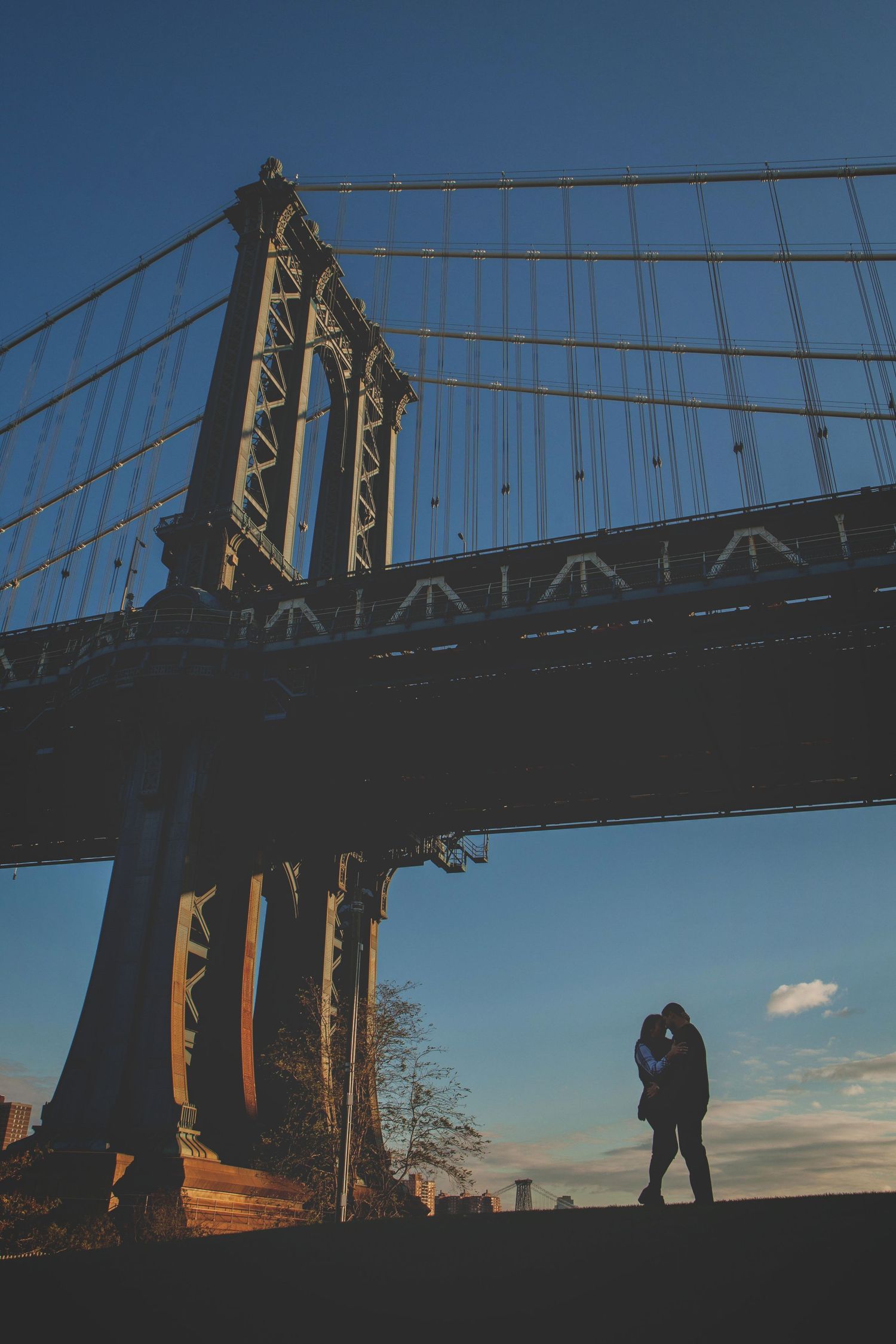 Couple standing in silhouette against a dramatic sunset backdrop of a bridge.