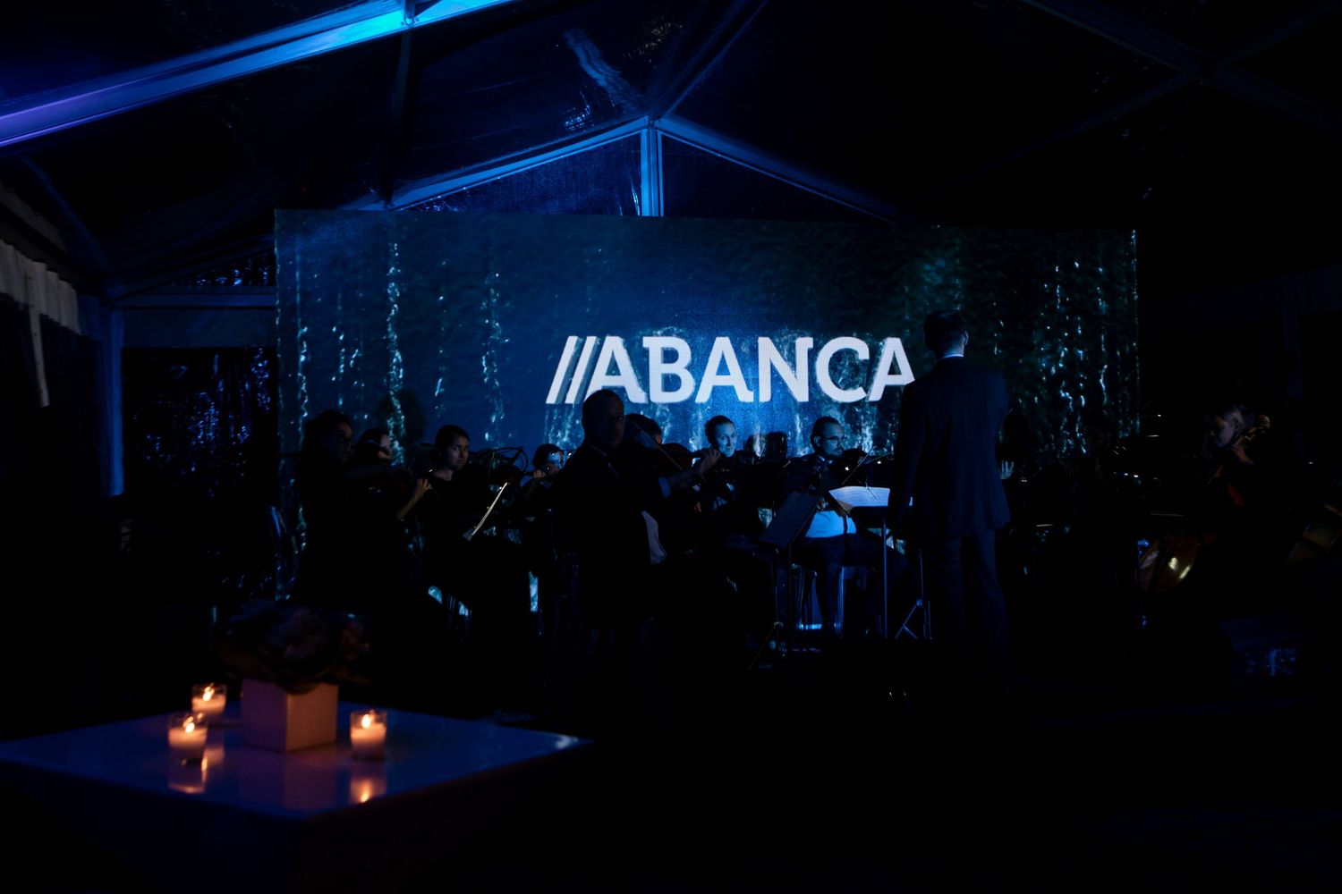Conference venue with illuminated Abanca company logo and dark blue lighting creating a dramatic atmosphere.