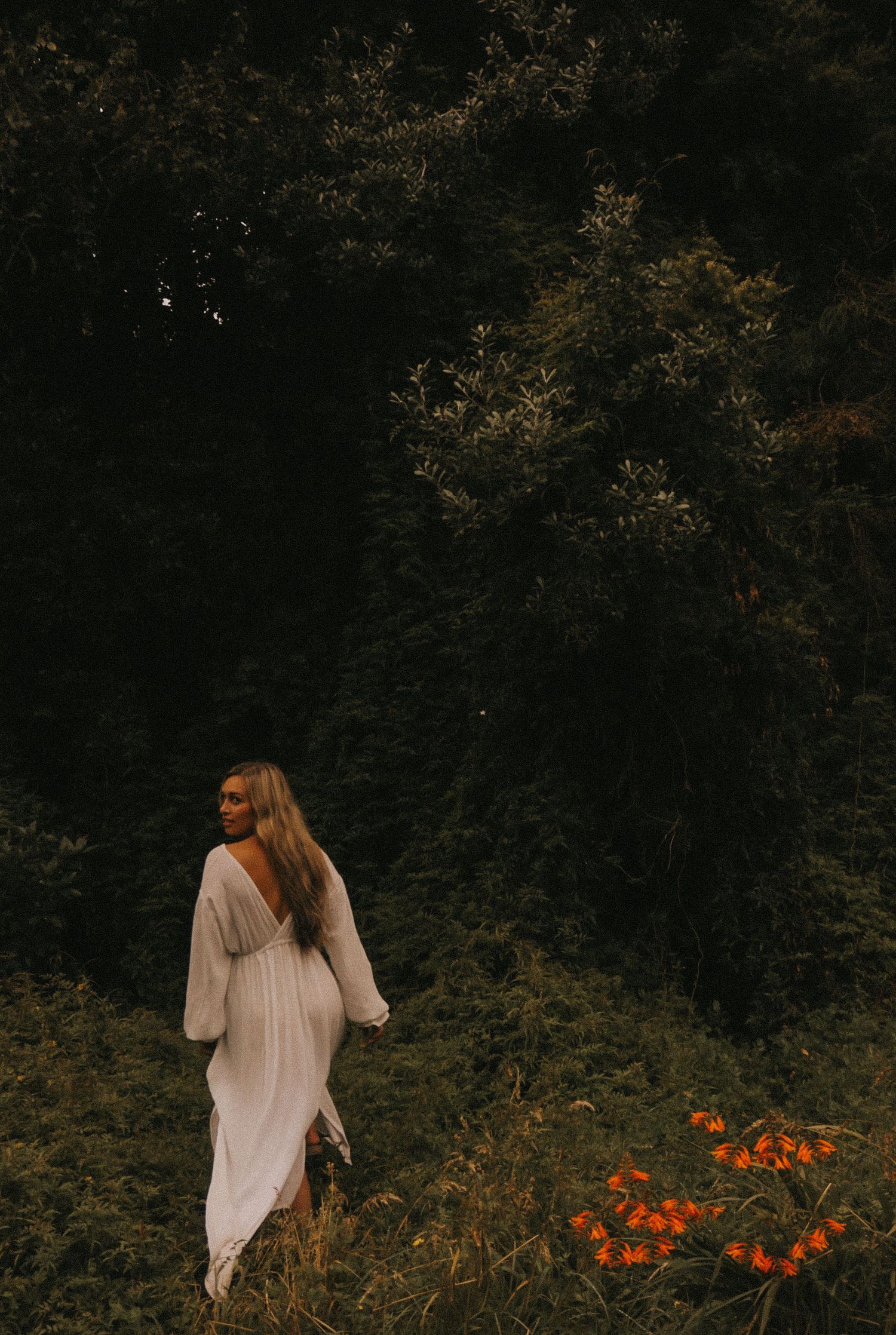 Woman in flowing white dress walking through garden with orange flowers.
