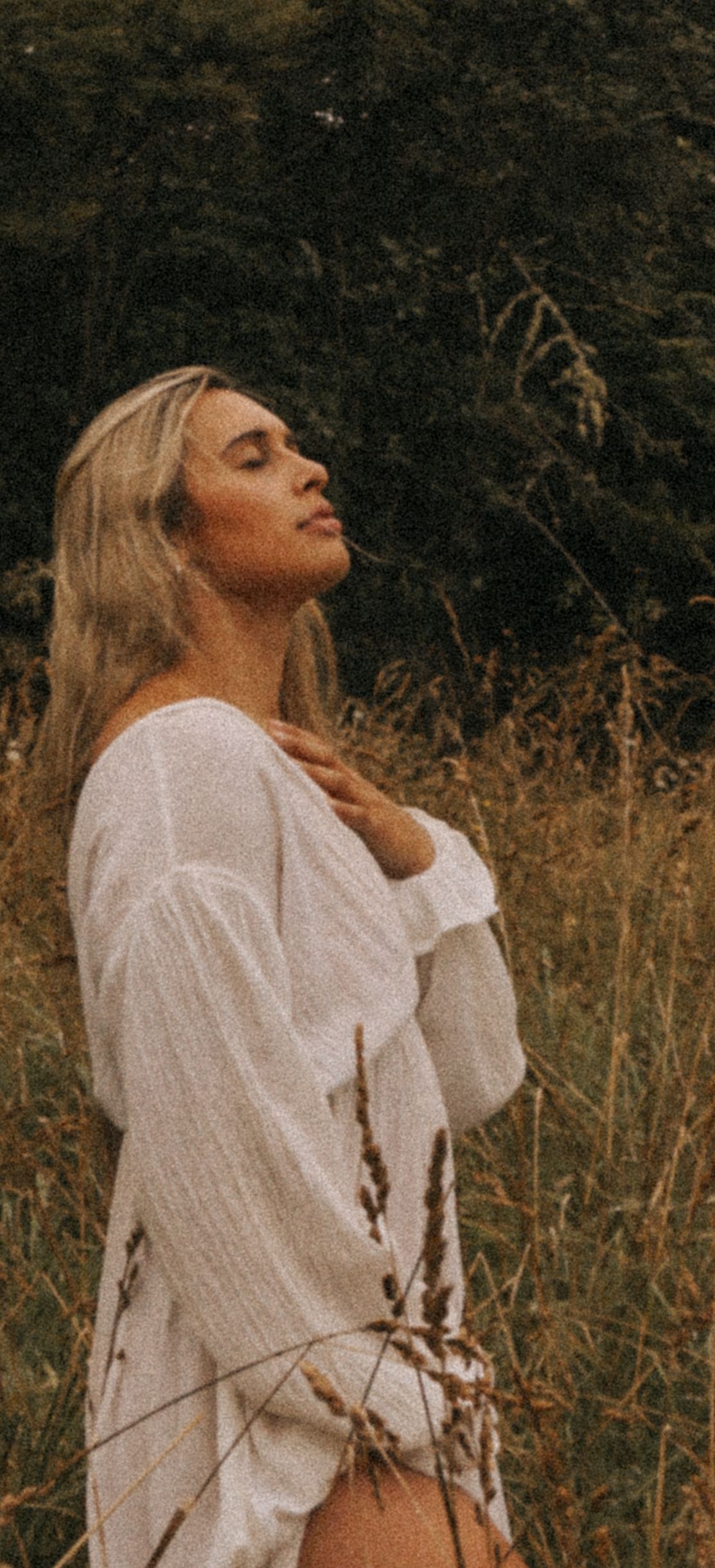 Person in white shirt poses dramatically against autumn field background.