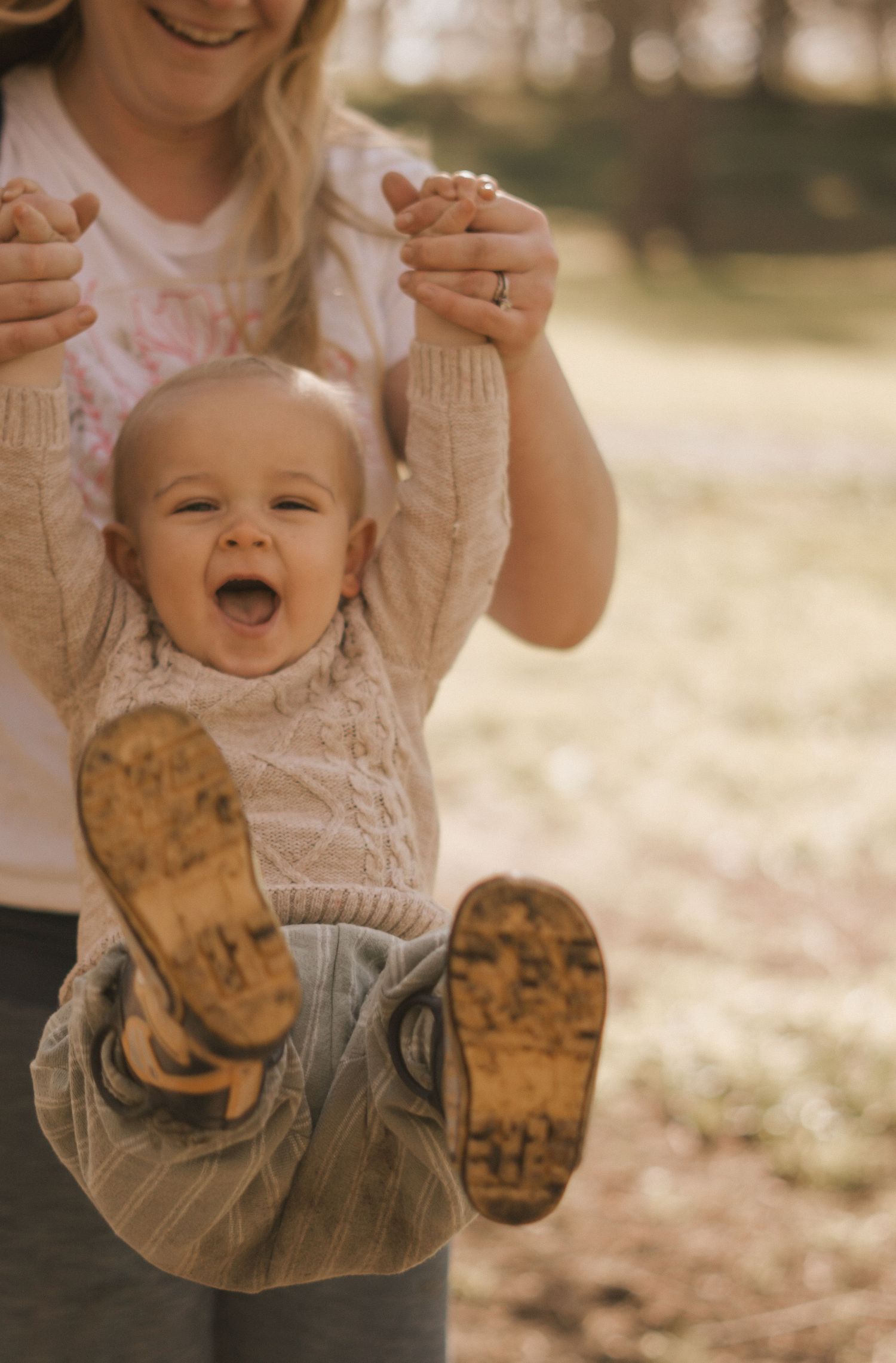 Baby in white lace outfit laughing while being held up against autumn backdrop.