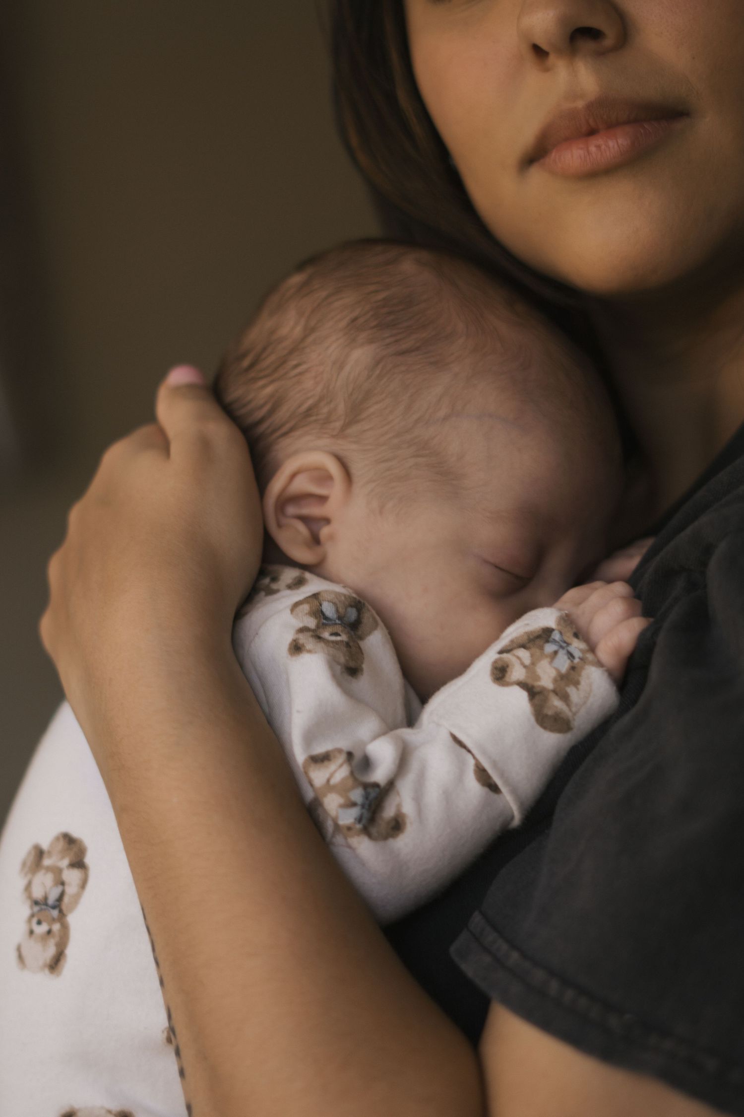 Close-up of sleeping infant in white onesie being cradled against dark clothing.