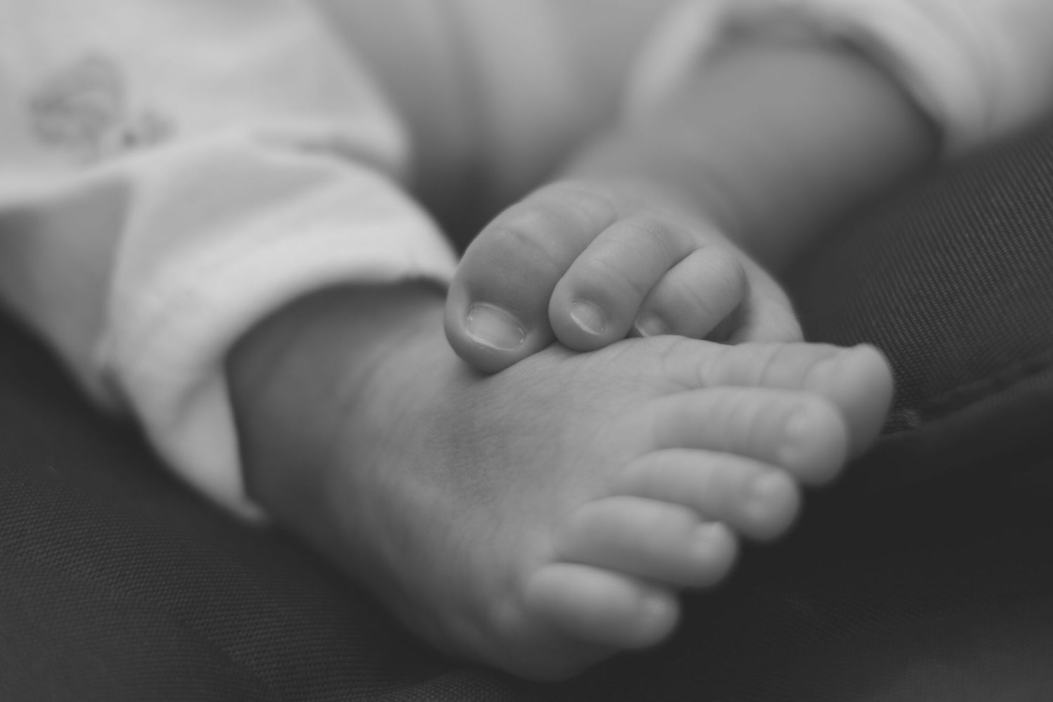 Close-up black and white image of feet gently touching.
