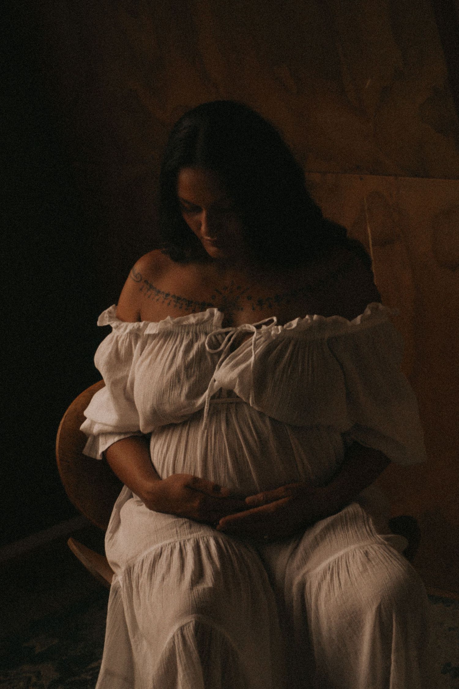 Dramatic side-view maternity portraits in dim lighting with white dress.