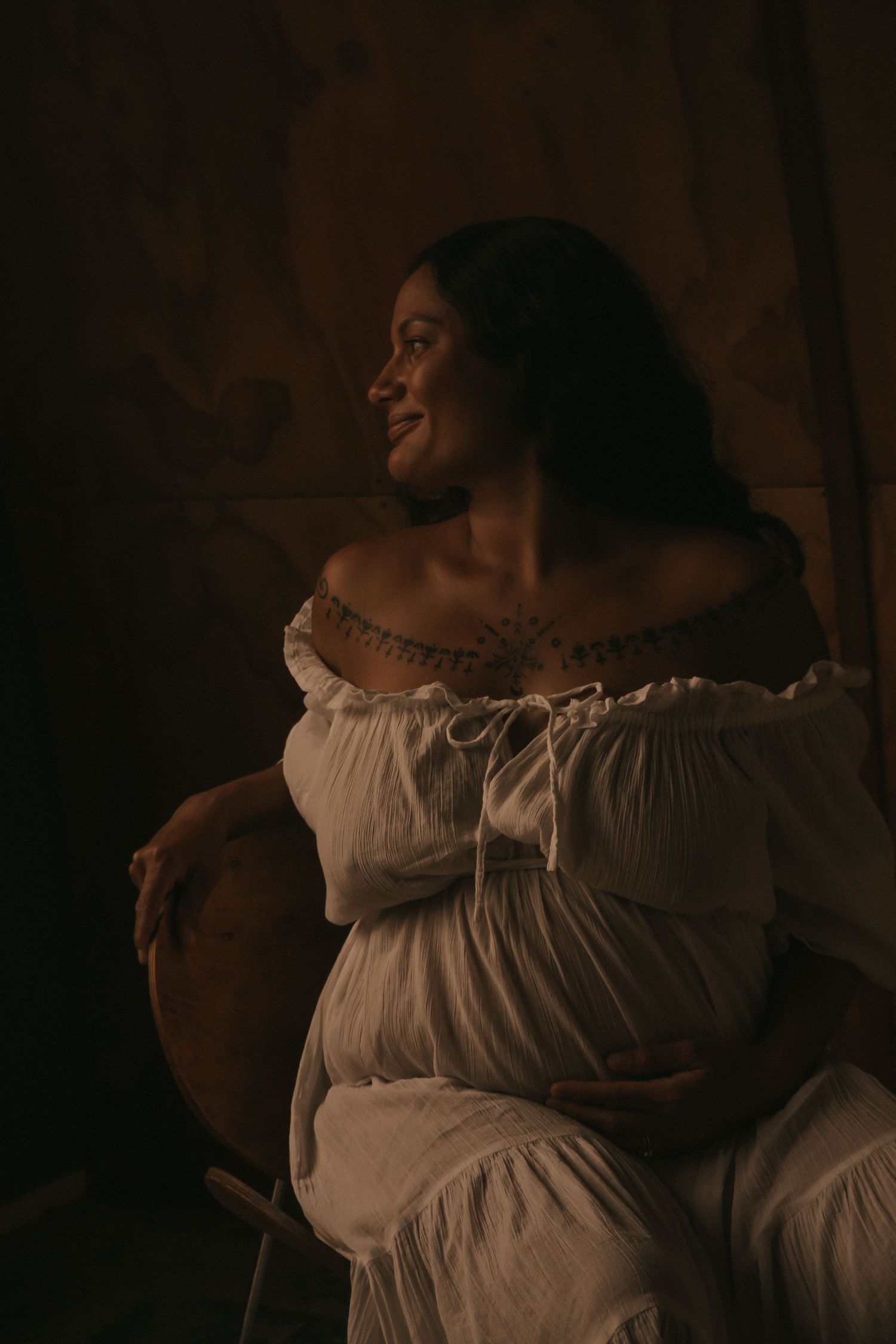 Moody maternity portraits in a white off-shoulder dress against dark background.
