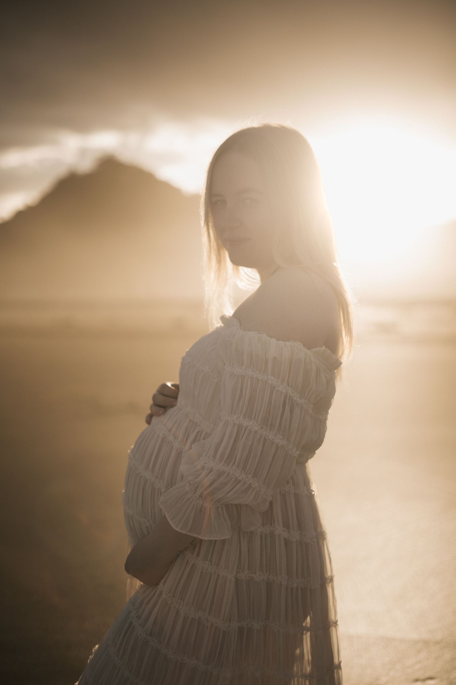 Silhouetted figures embrace in warm golden sunlight creating a romantic backlit scene at sunset.
