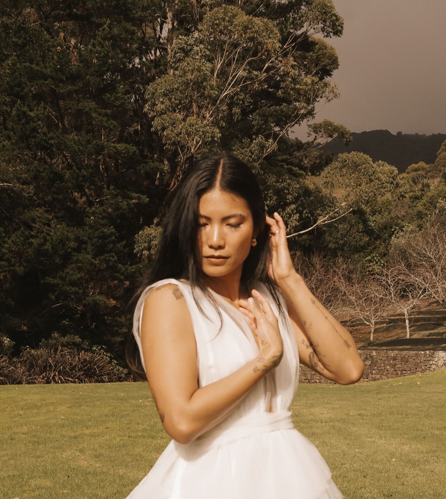 Figure in white dress poses gracefully on grassy hillside during golden hour.