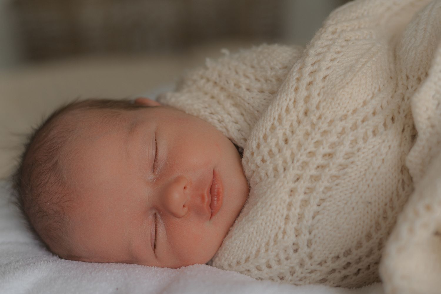 A peaceful newborn baby sleeps soundly wrapped in a cozy white knit blanket.