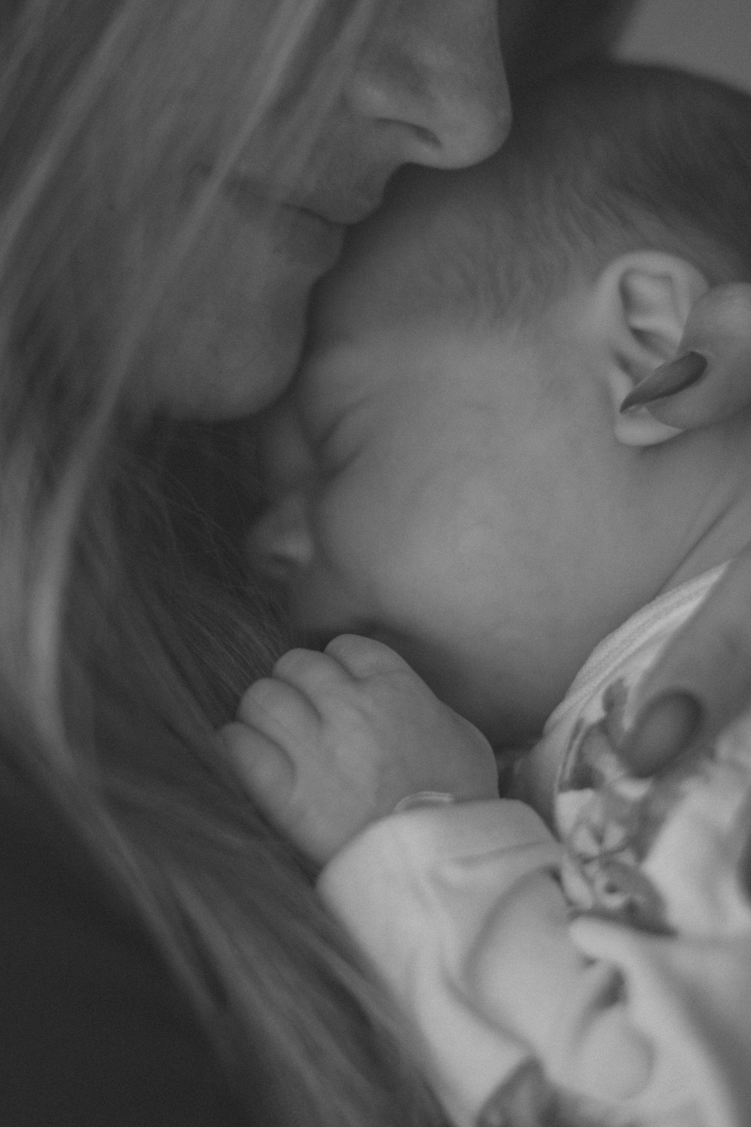 Black and white close-up of sleeping newborn being gently held.