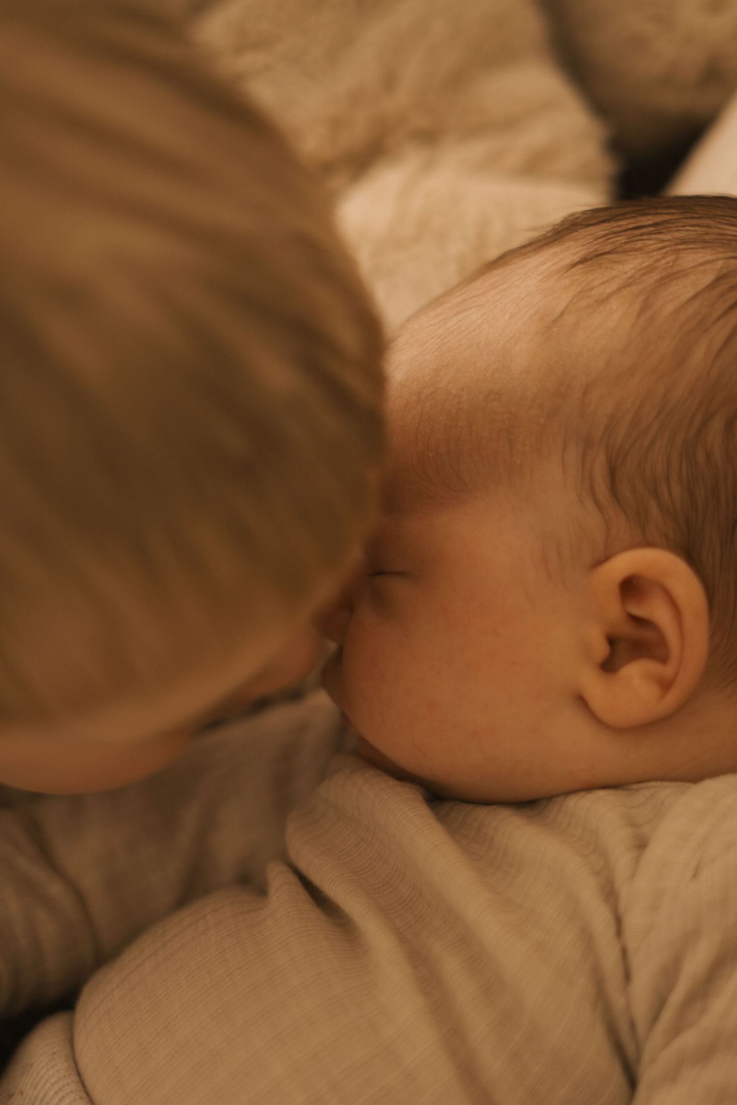 Side profile of sleeping baby resting on soft beige surface.