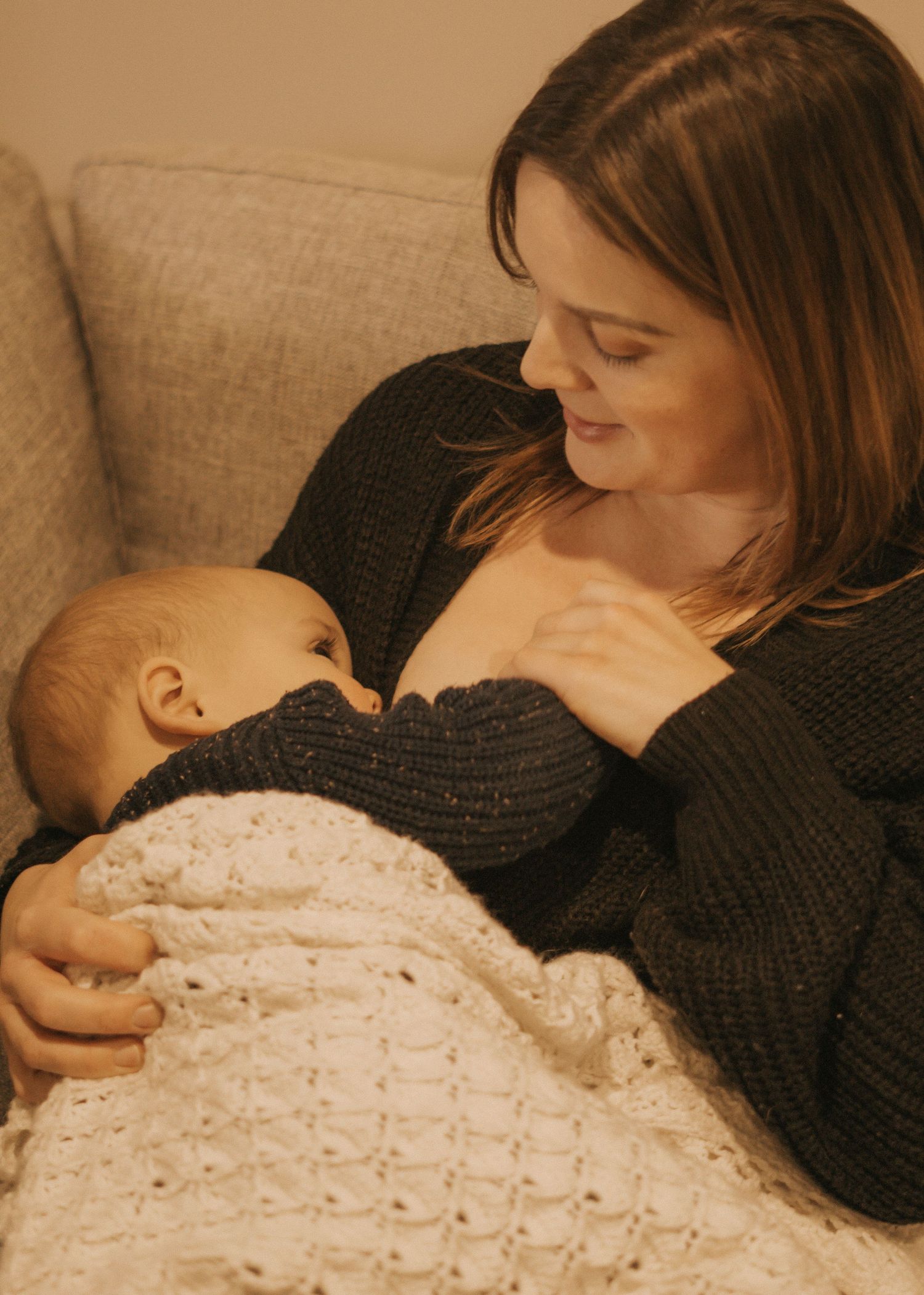 Parent cradling sleeping baby wrapped in white knitted blanket.
