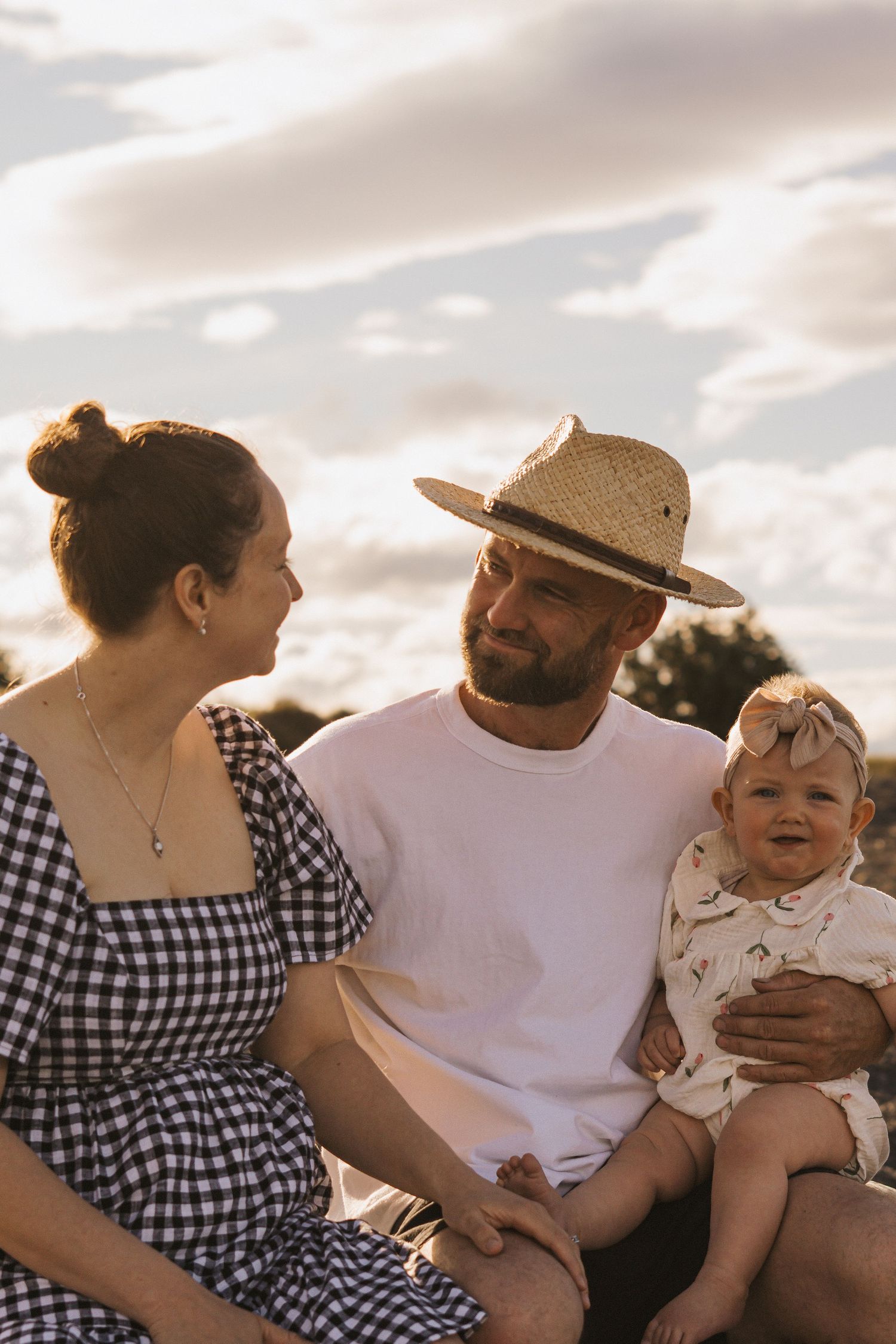 Family sitting together outdoors during golden hour, wearing casual clothes and sharing joyful moments.