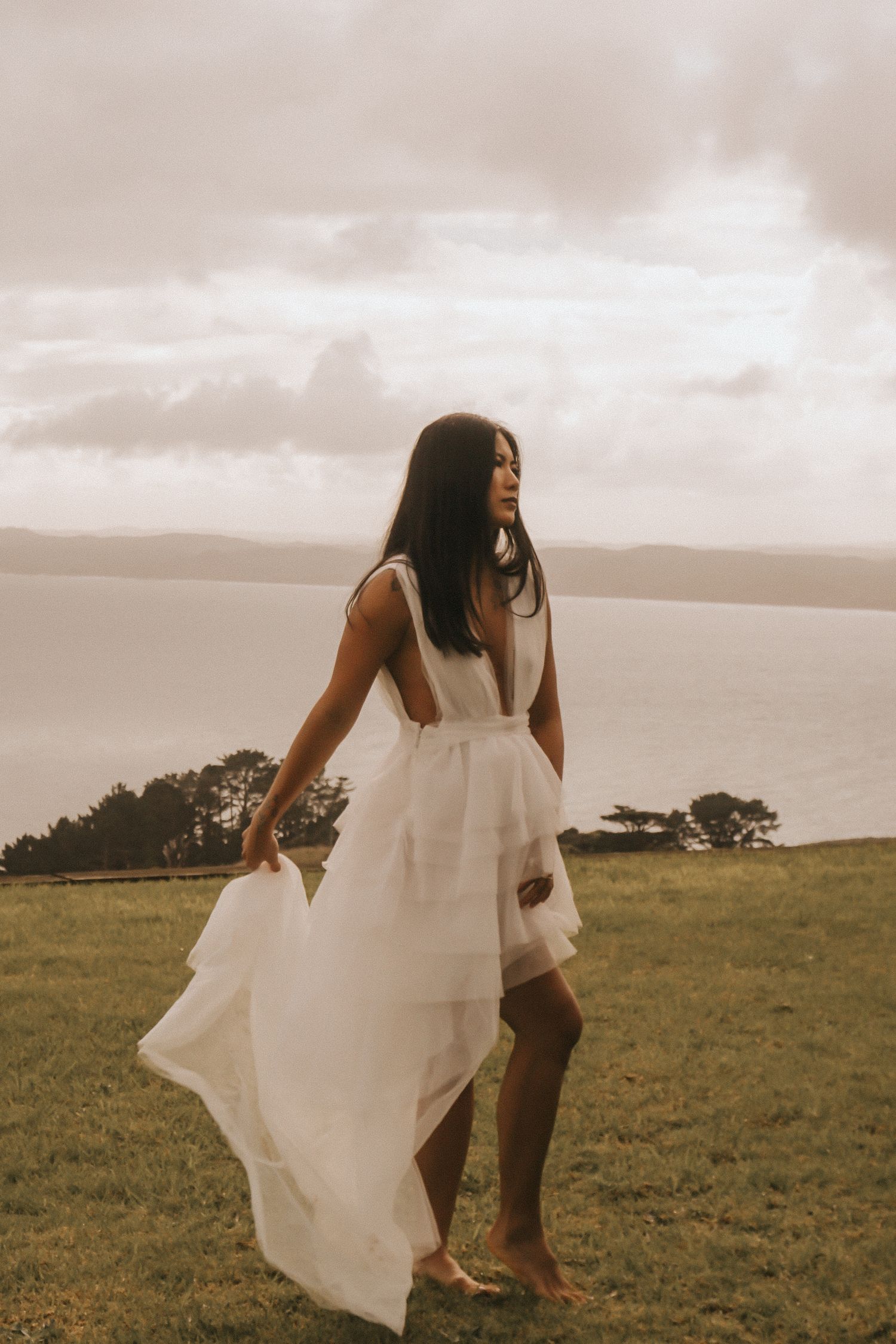 Figure in billowing white dress dances across coastal grassland with ocean view.