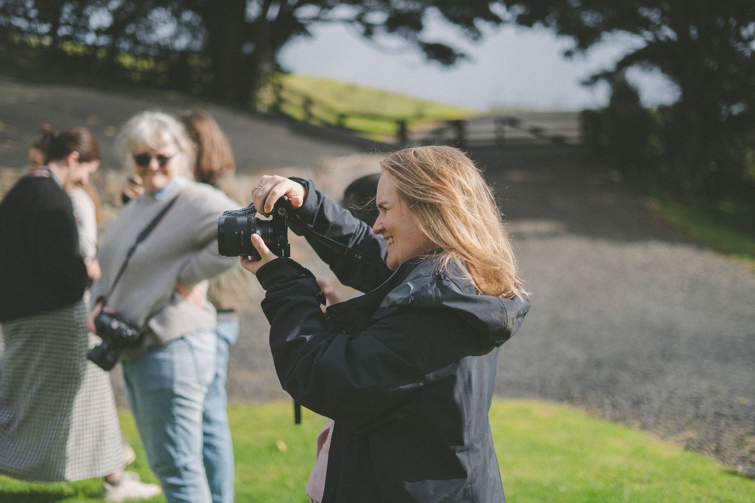People taking photos outdoors on a sunny day with cameras and phones.