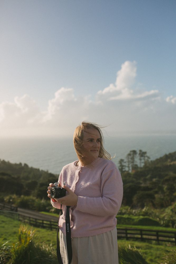 Person in pink sweater photographs scenic mountain landscape at sunset.