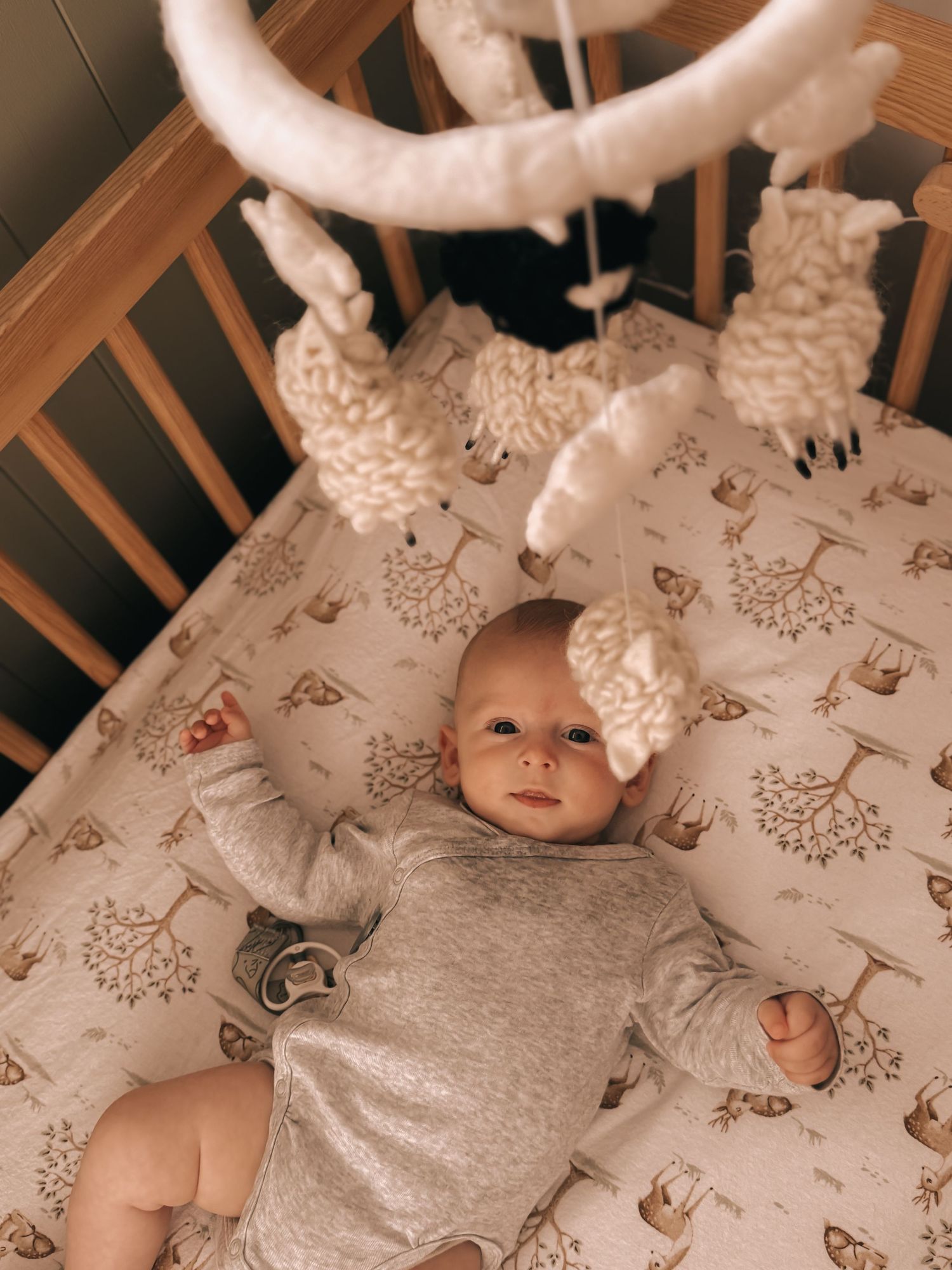 A baby lies on patterned bedding in a wooden crib.