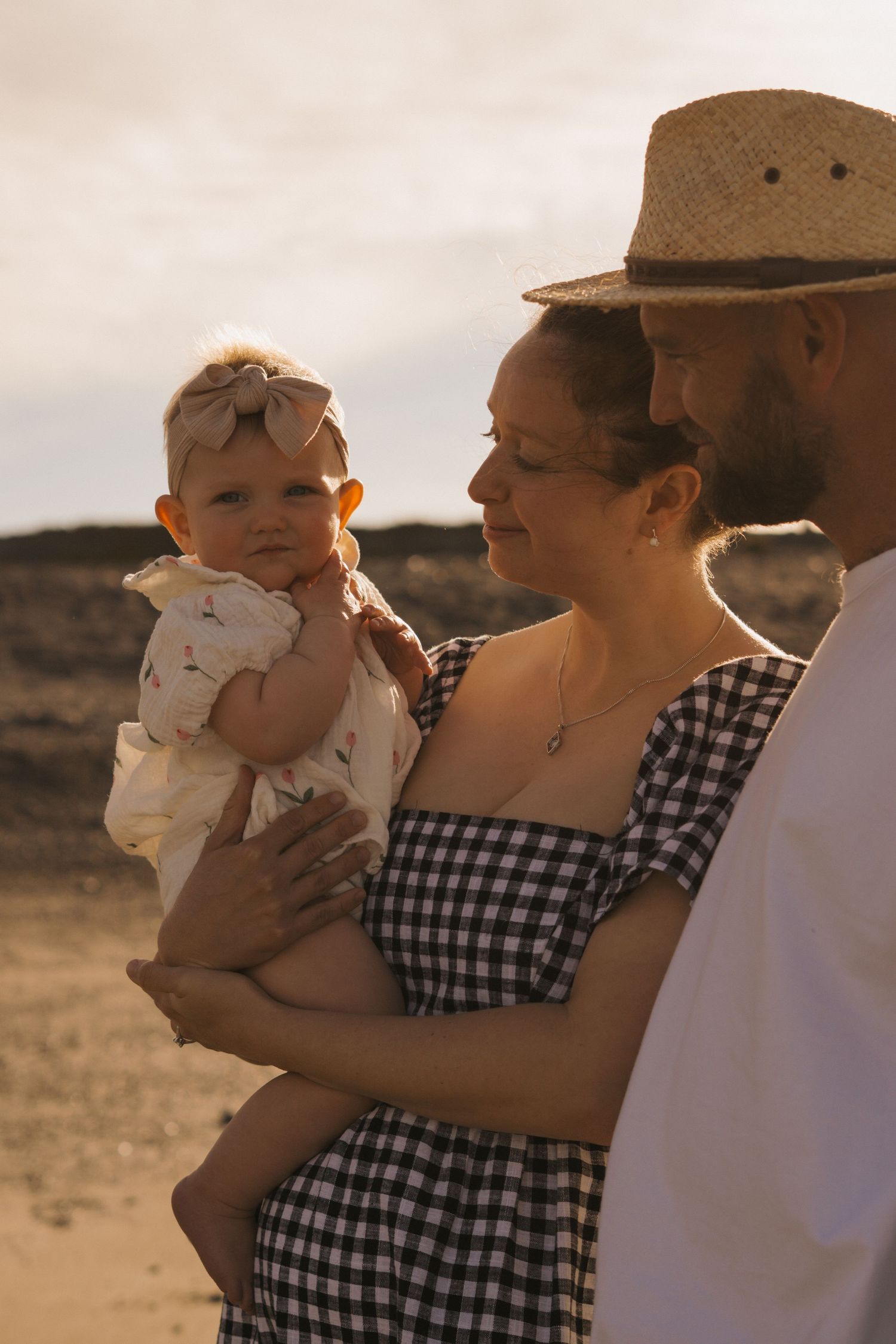 A family in gingham dress and cowboy hats stands together against a desert landscape at sunset.