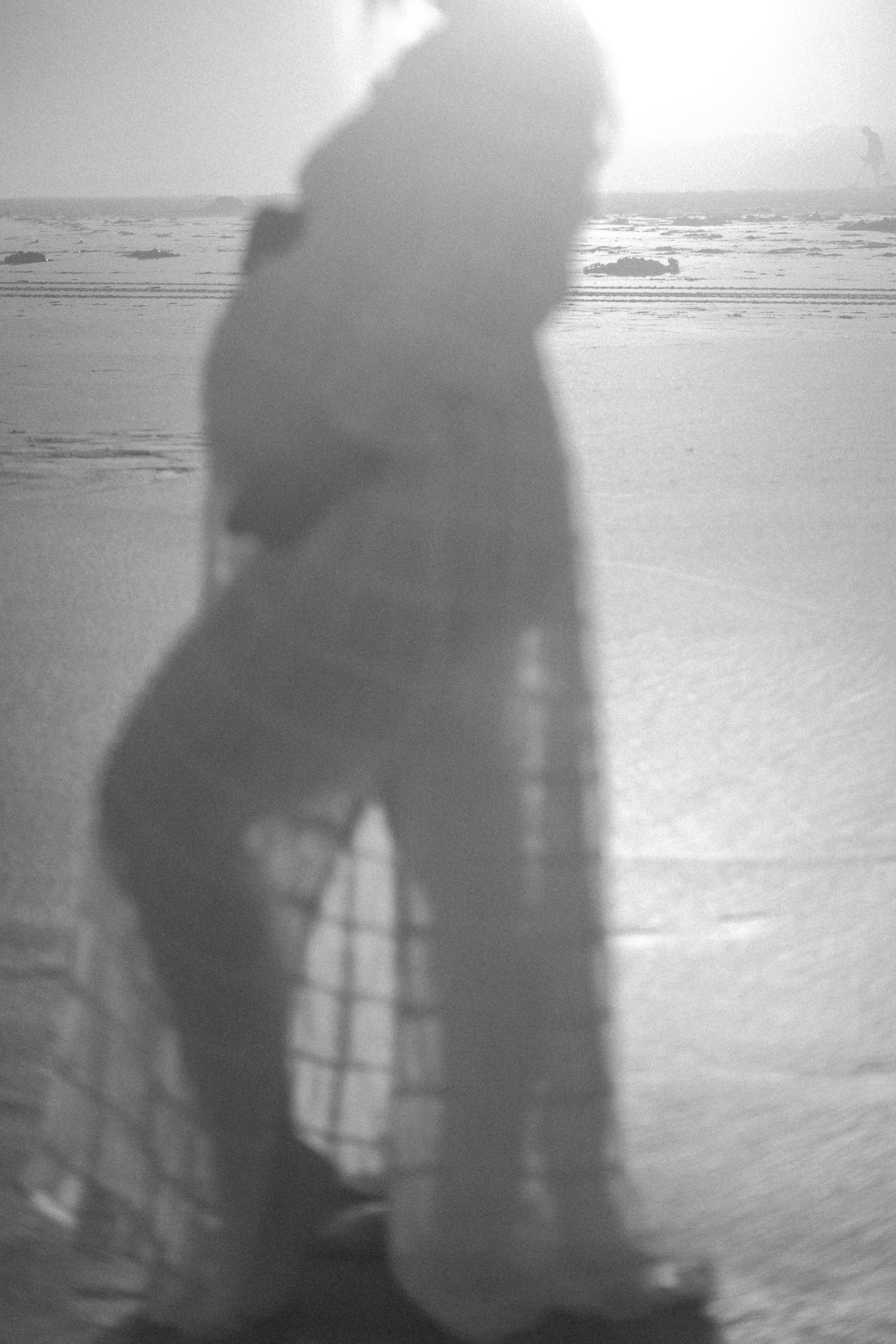 A blurry black and white silhouette of a person standing on a beach with waves in the background.