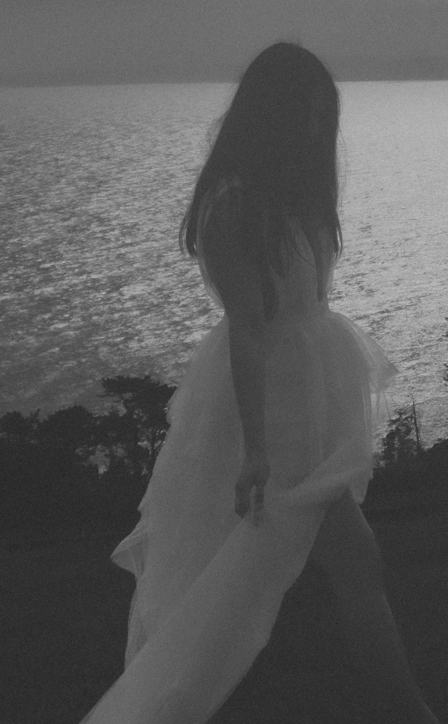 Silhouetted figure in white dress against dramatic ocean backdrop at sunset.