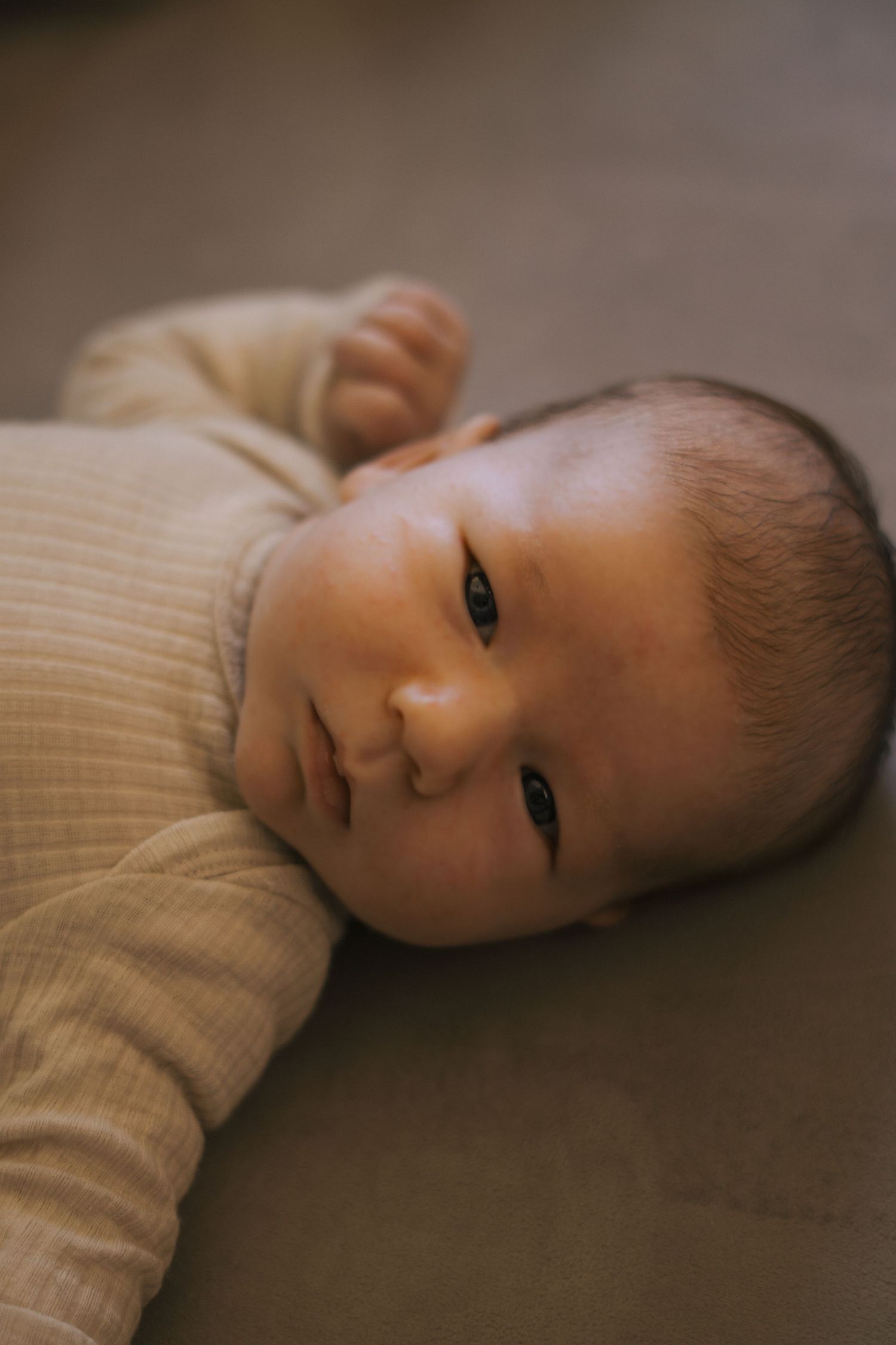 Baby in white sweater lying on brown surface looking at camera.