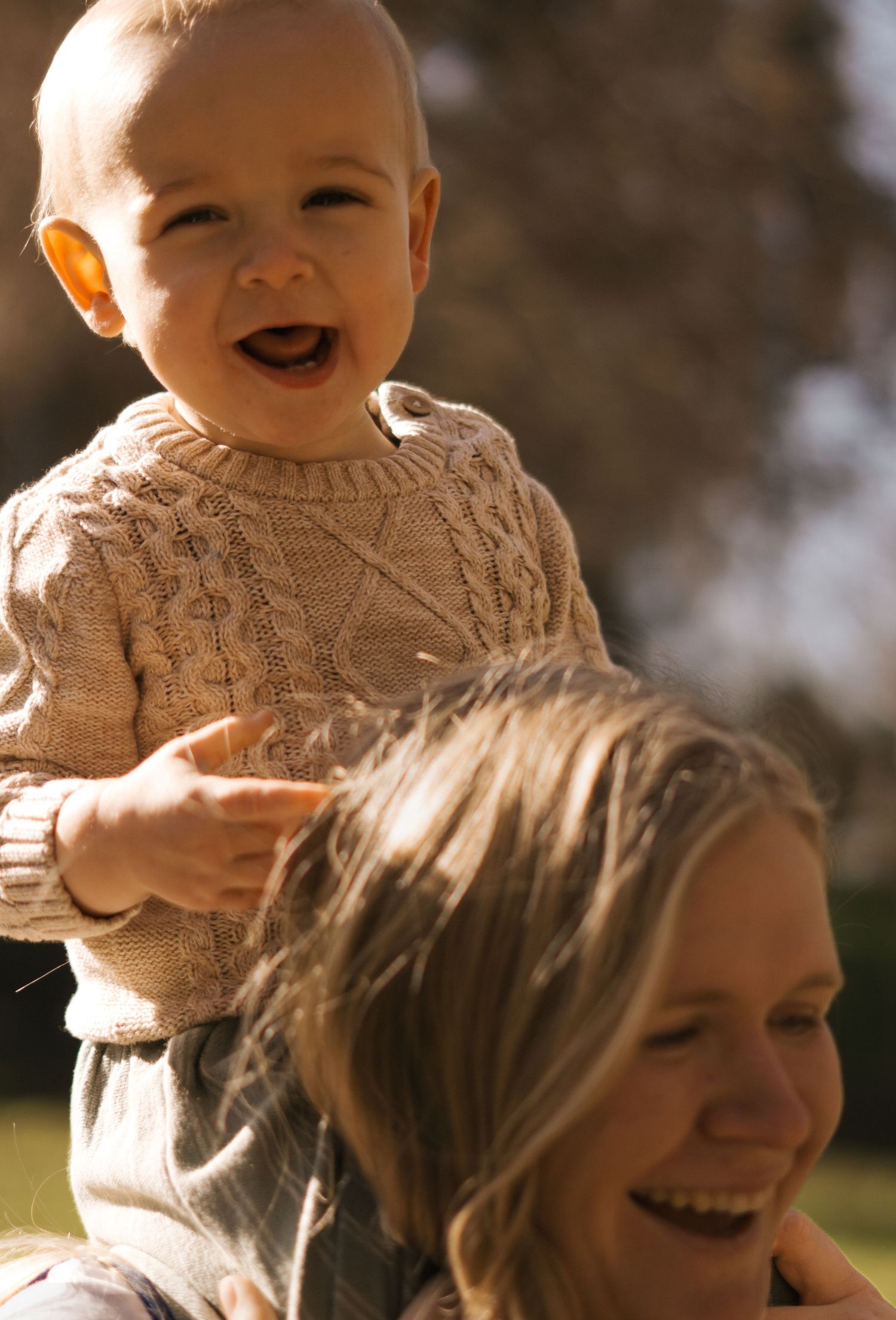 Candid outdoor portrait of joyful moments between parent and baby in knit sweater.