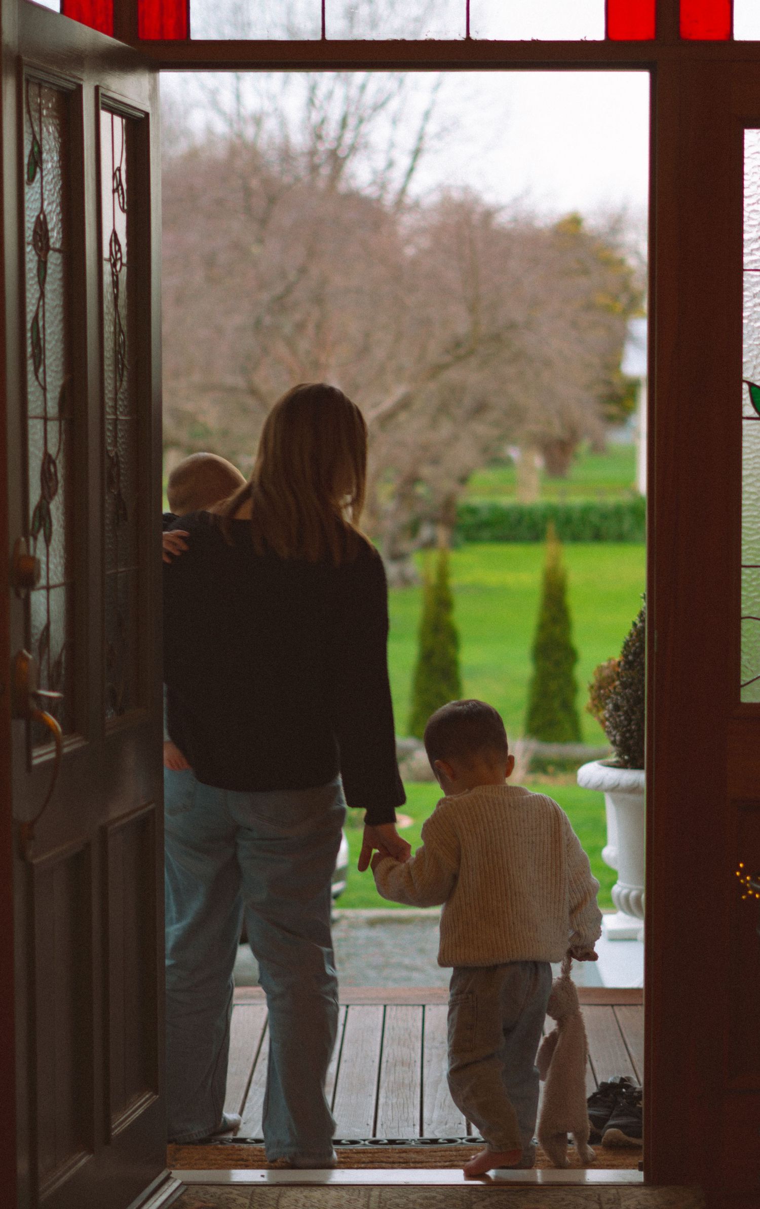 Silhouetted figures walking through a doorway with red accents and outdoor view.