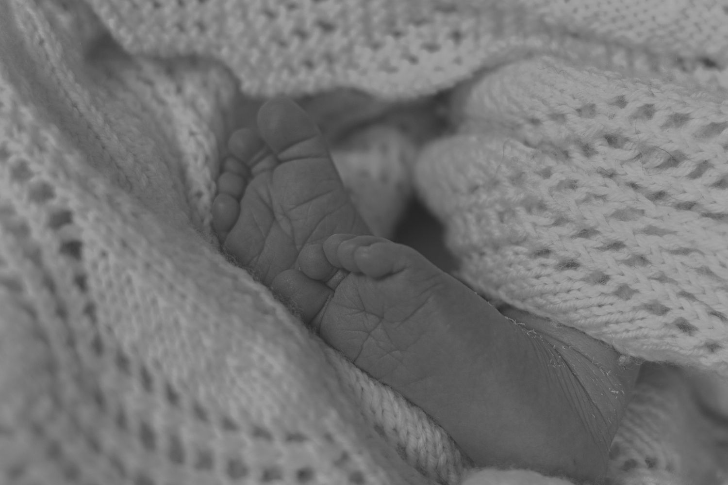 A tiny baby's hand grasps a soft knitted white blanket in a tender close-up shot.