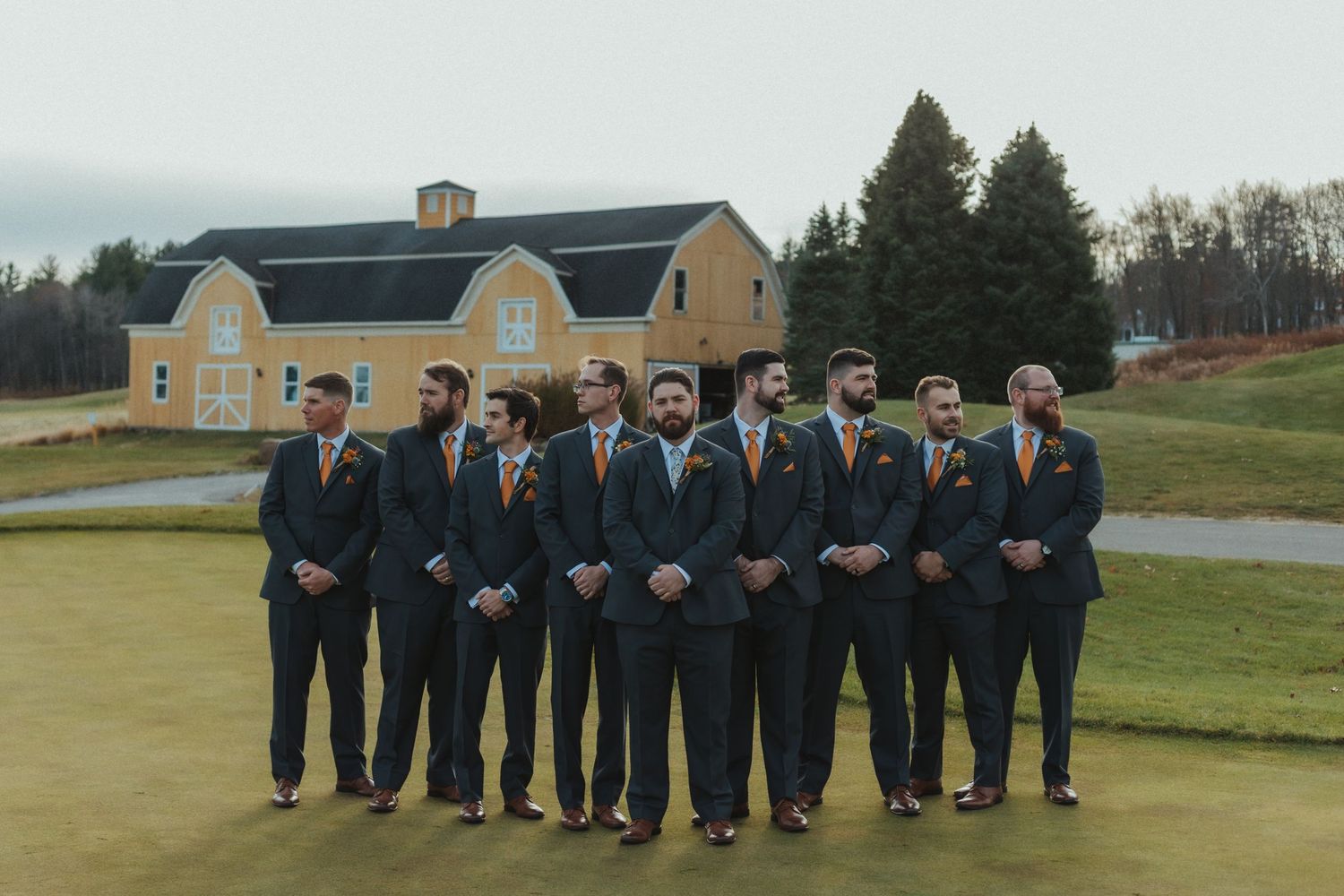 Groomsmen in navy suits pose together on a golf course for a wedding photo.
