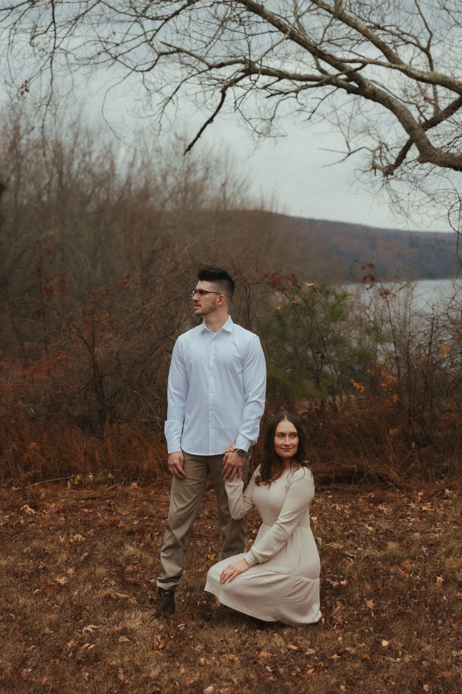 A couple sits together on an autumn hillside overlooking a scenic lake view.