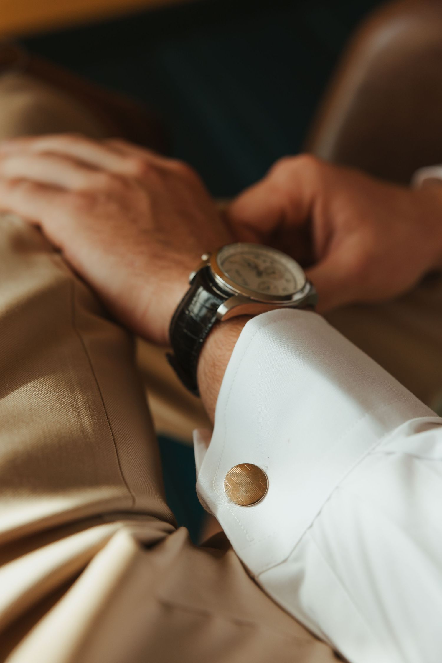 Close-up view of hands adjusting white dress shirt cuffs with a sleek wristwatch visible.
