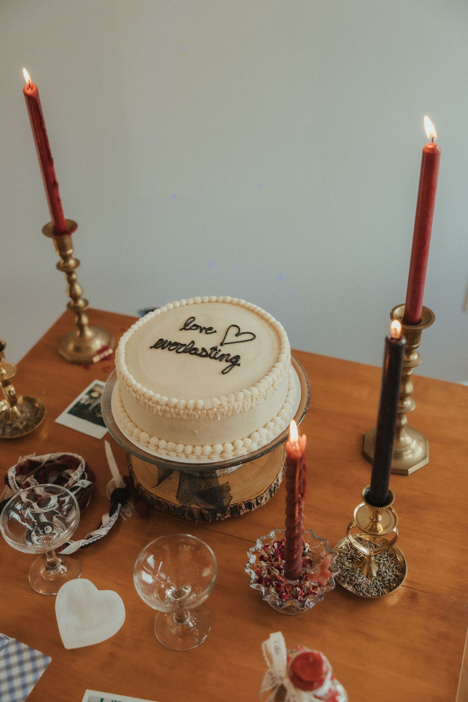 A white frosted cake with candles displayed on a wooden table with vintage brass candlesticks.