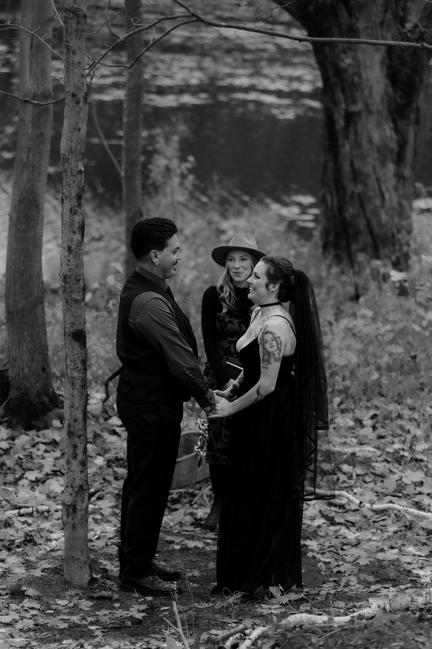 Black and white photo series showing two small children in dark coats playing in fallen autumn leaves in a forest.