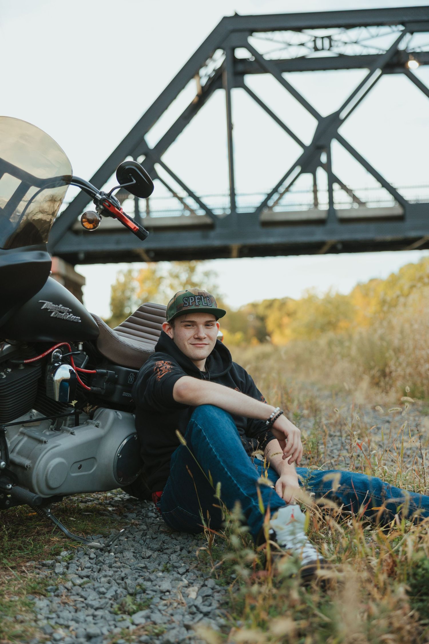 Young person in casual attire reclining by railroad tracks during golden hour in autumn setting.